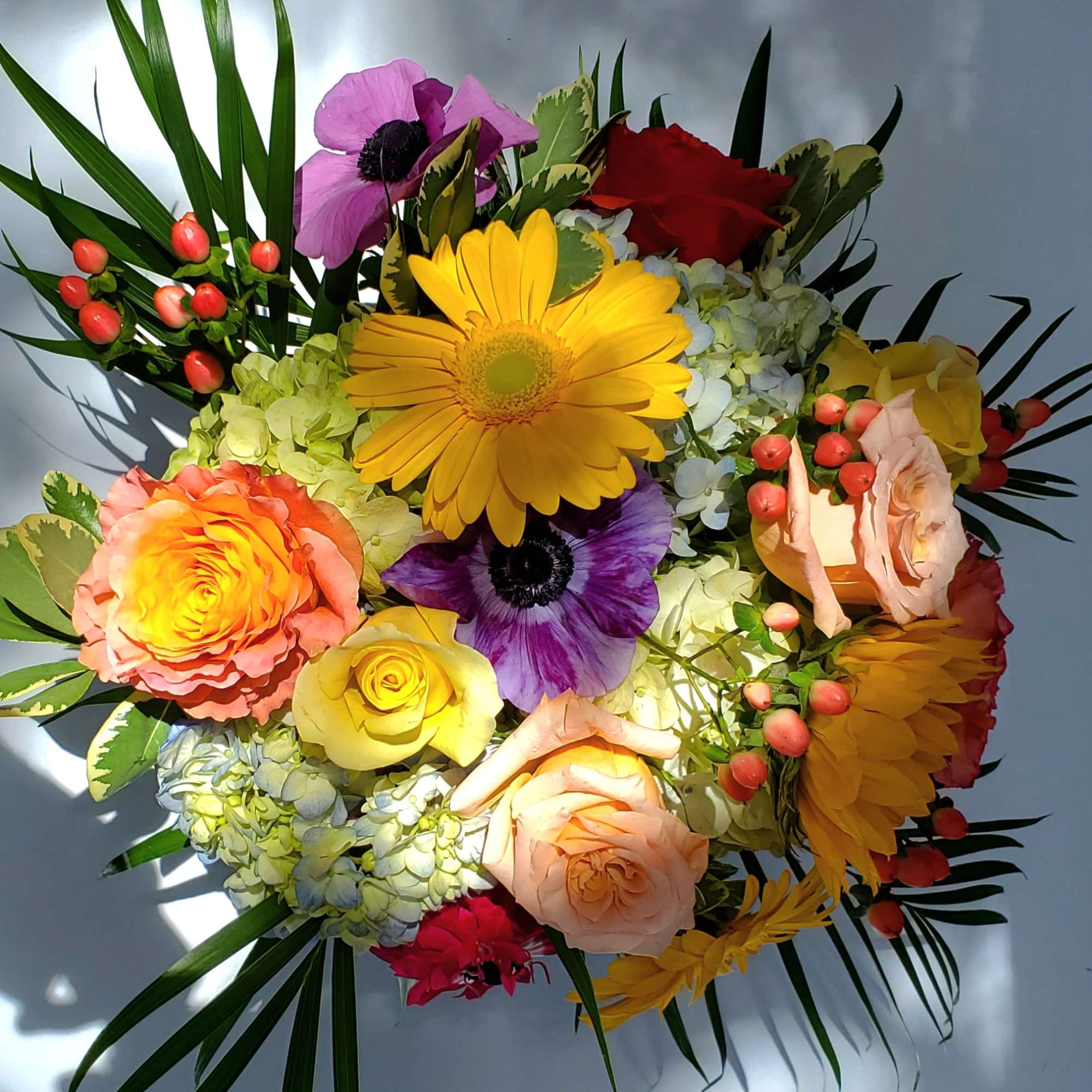 Colorful mixed bouquet with yellow gerbera daisies, roses, hydrangea, and purple anemones