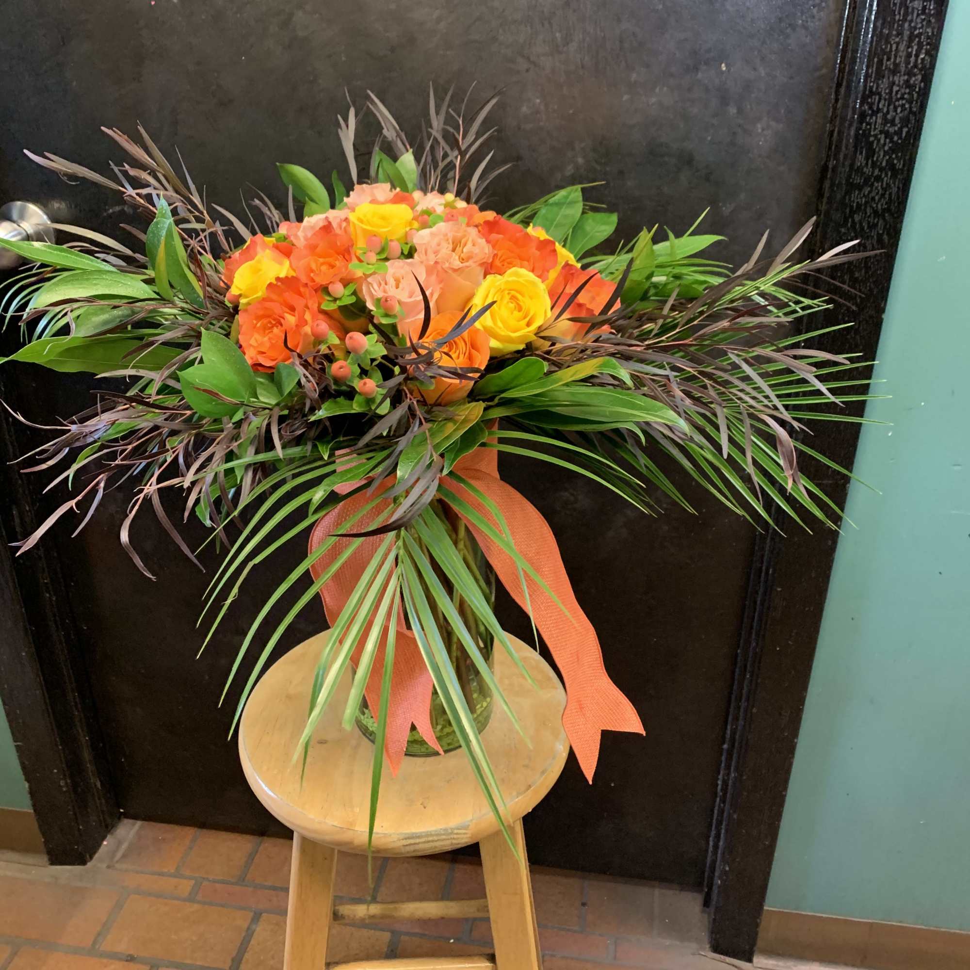 Orange and yellow rose bouquet in a glass vase with a ribbon