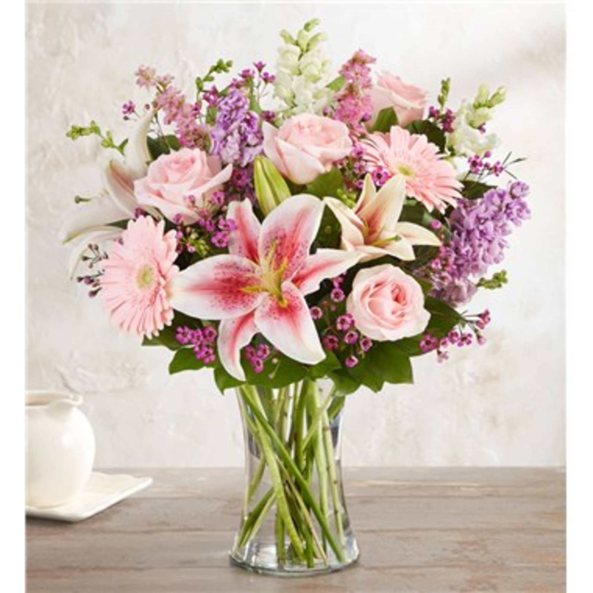 Mixed bouquet of pink lilies, roses, gerbera daisies and purple blooms in a clear glass vase