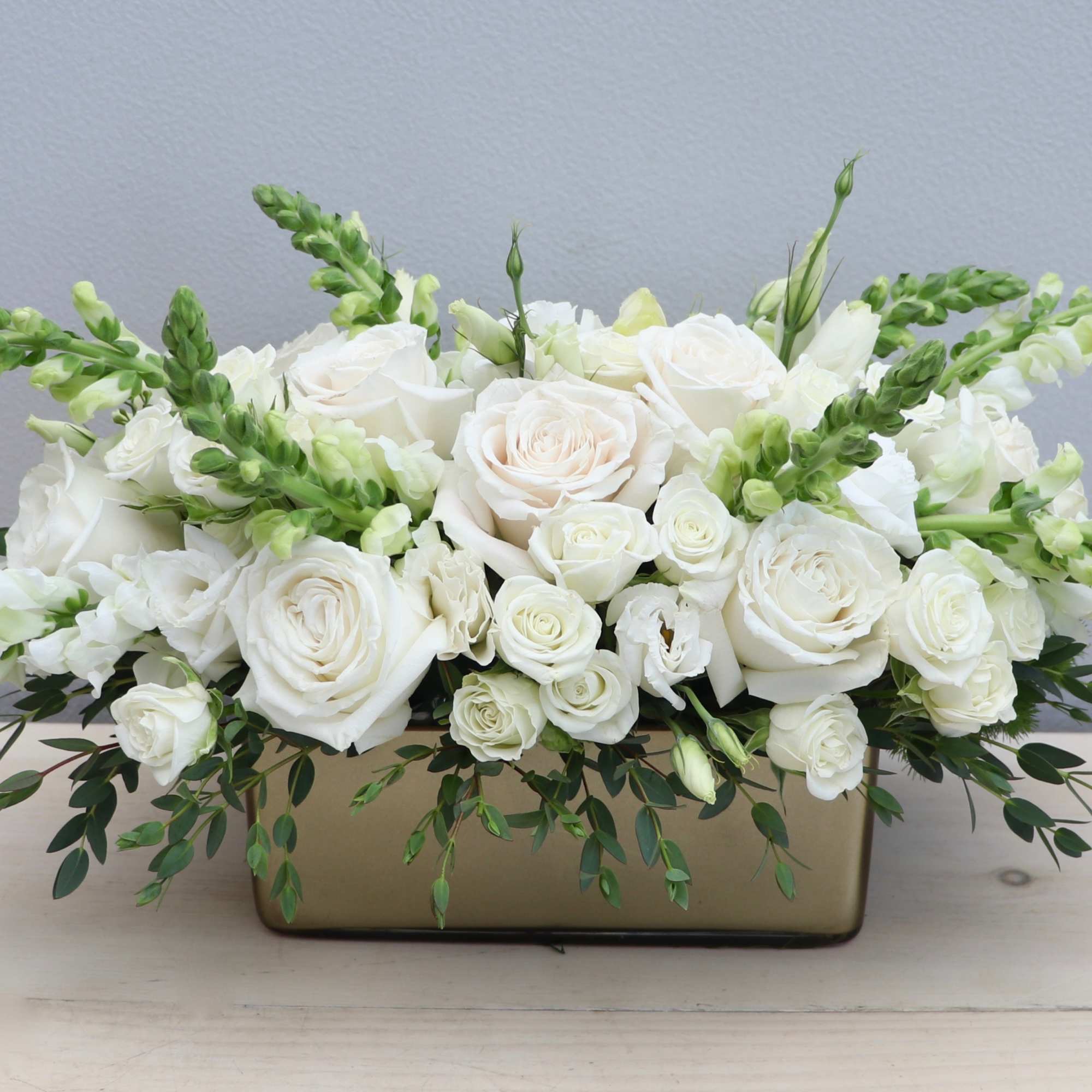 Low white rose and snapdragon arrangement in a rectangular gold vase
