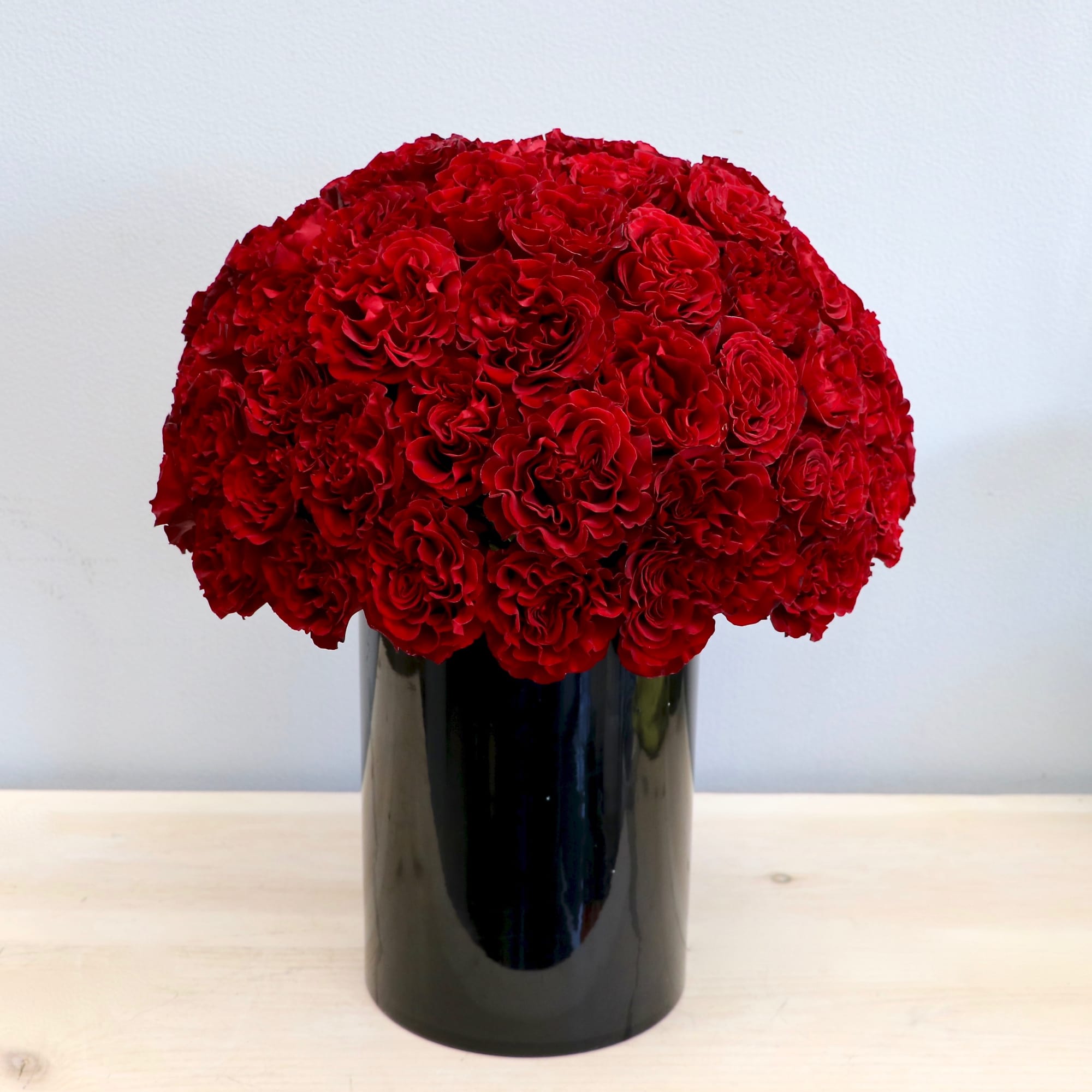 Dome of red carnations tightly arranged in a tall glossy black cylinder vase