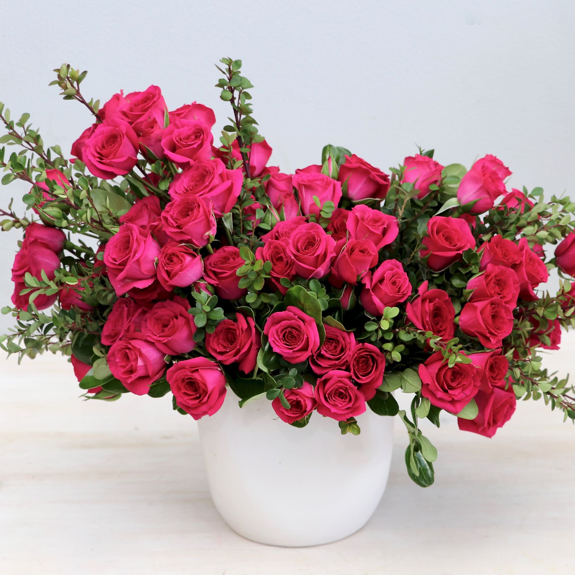 Lush arrangement of hot pink roses with green accents in a white ceramic pot