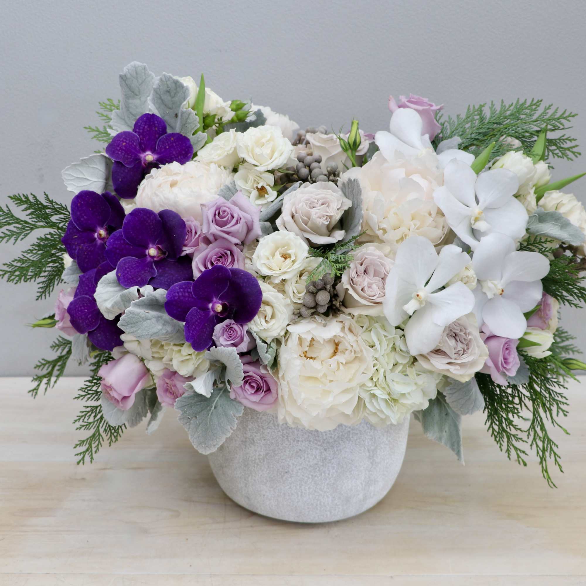 Low white vase of white and blush flowers with purple and white orchids and soft greenery.