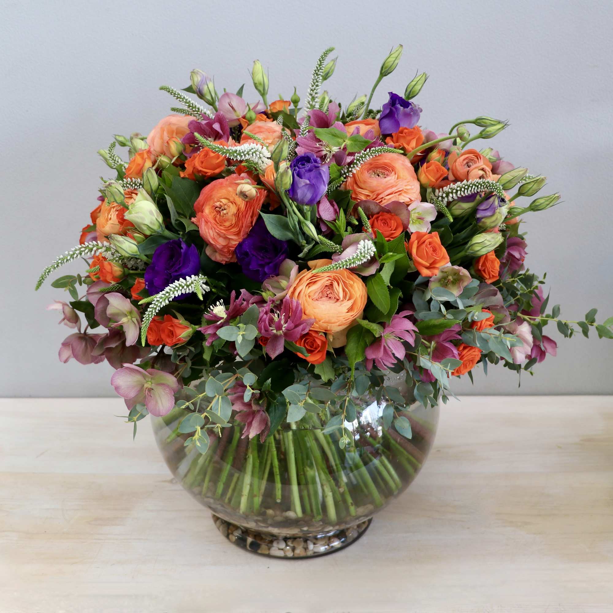 Low round arrangement of orange and purple flowers in a clear fishbowl glass vase