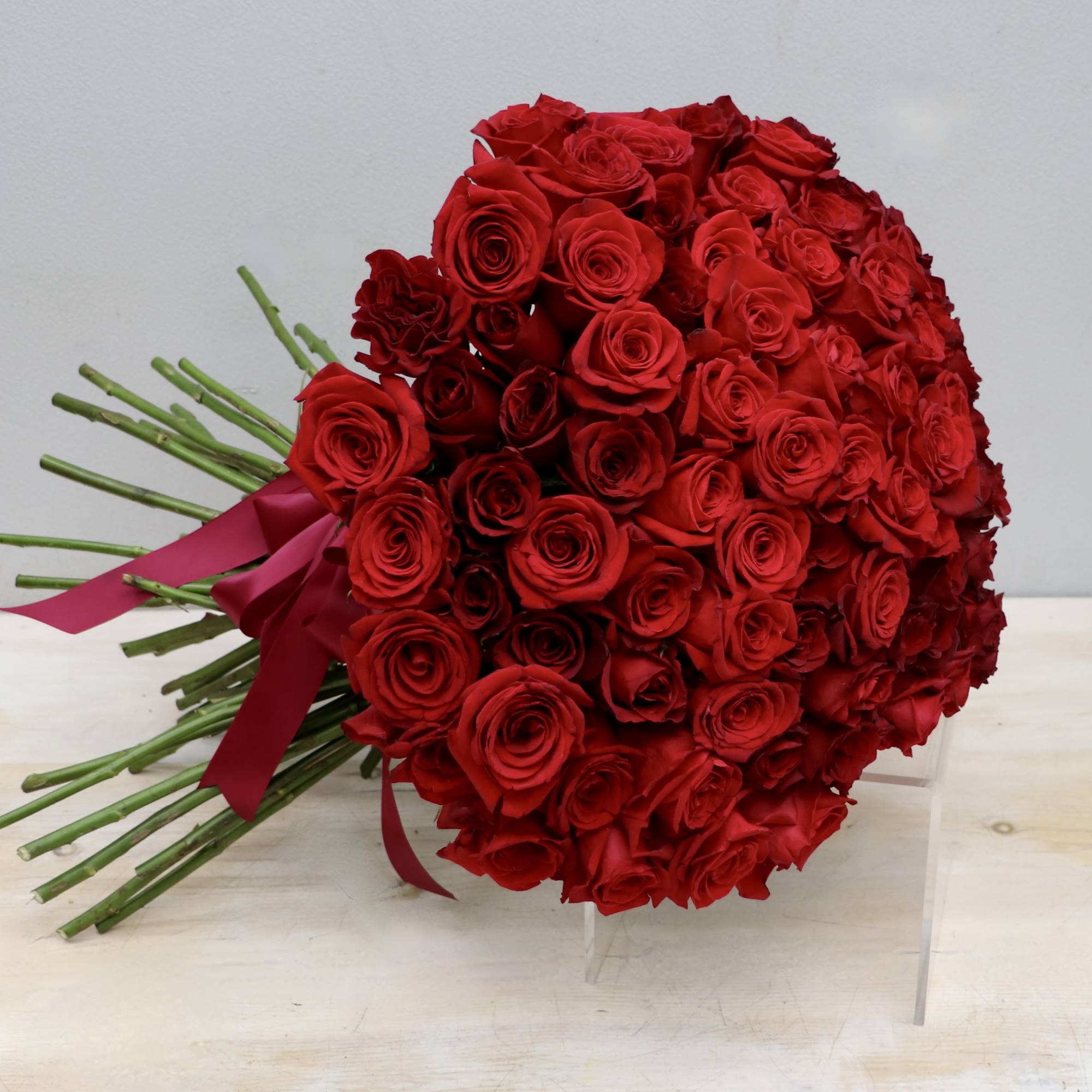 Large hand-tied bouquet of tightly packed red roses with long stems and red ribbon