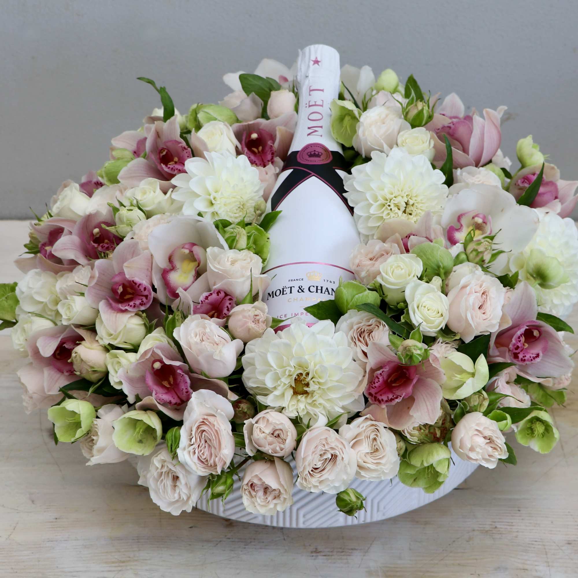 Low round arrangement of pink and white flowers with a Moët champagne bottle in a white bowl