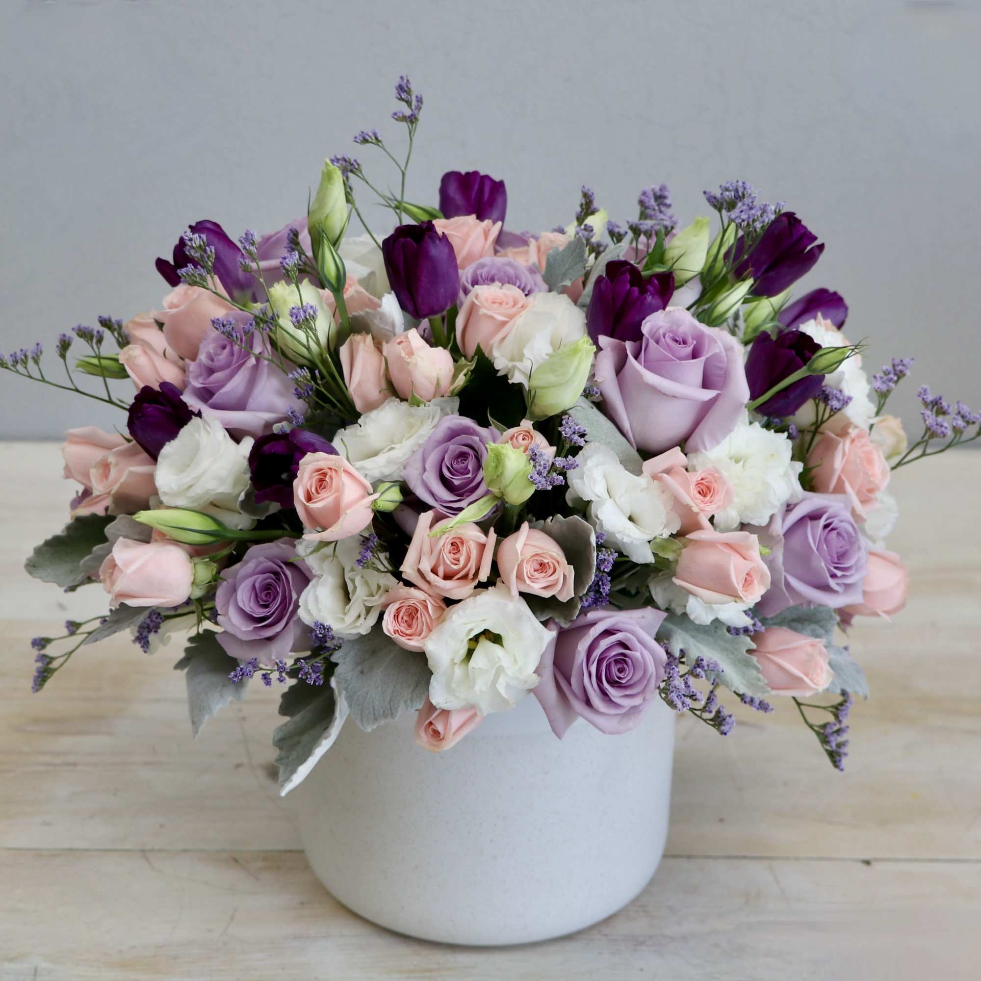Low pastel arrangement of pink and lavender roses with white blooms in a white ceramic pot