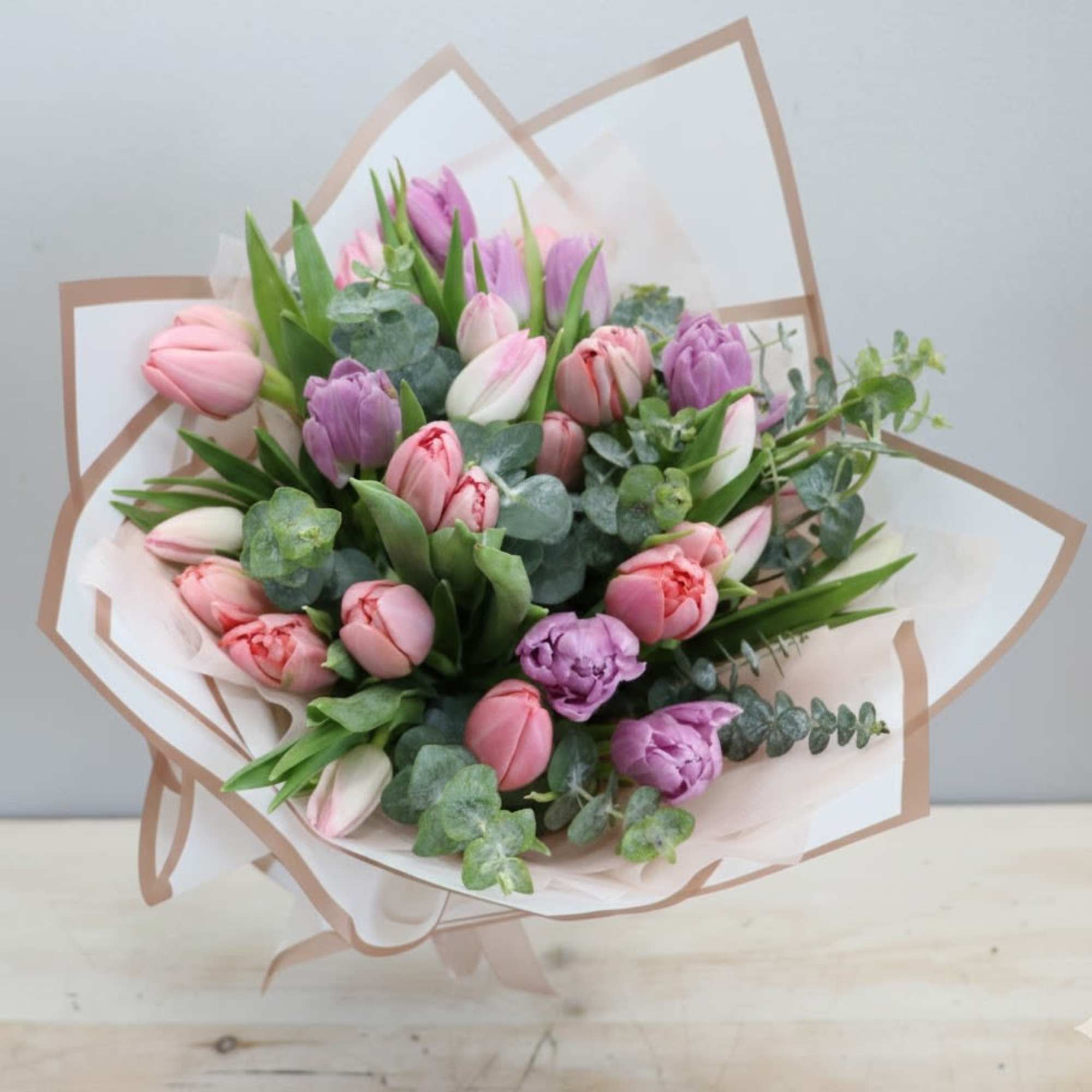 Hand-tied bouquet of pink and purple tulips with eucalyptus wrapped in white and beige paper.