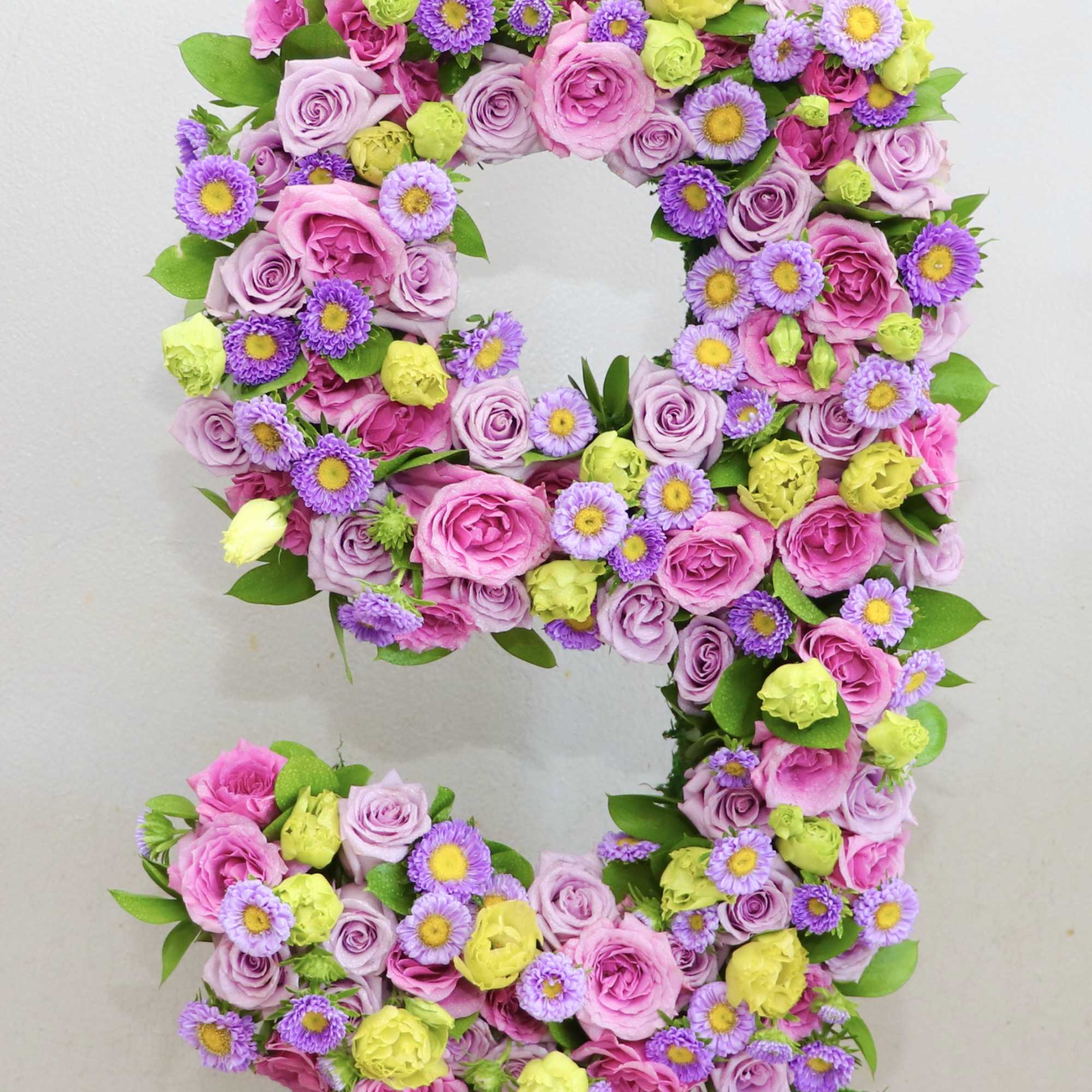 Floral number 9 made of pink, purple, and yellow flowers in a moss-covered base