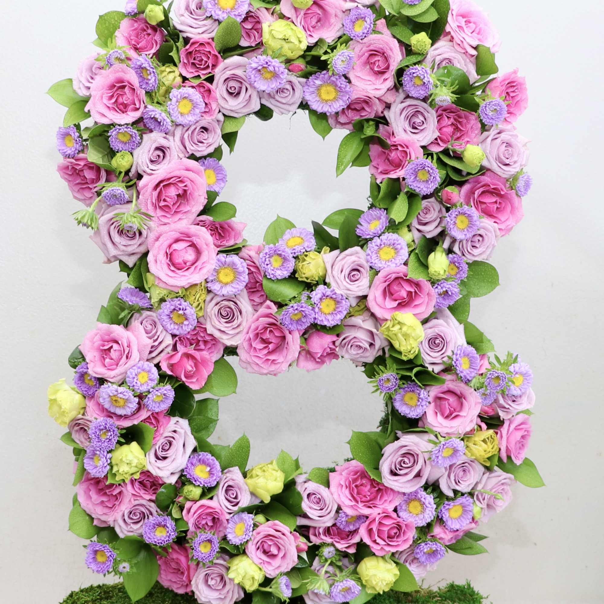 Pink and lavender floral wreath with small purple daisies on a moss-covered base