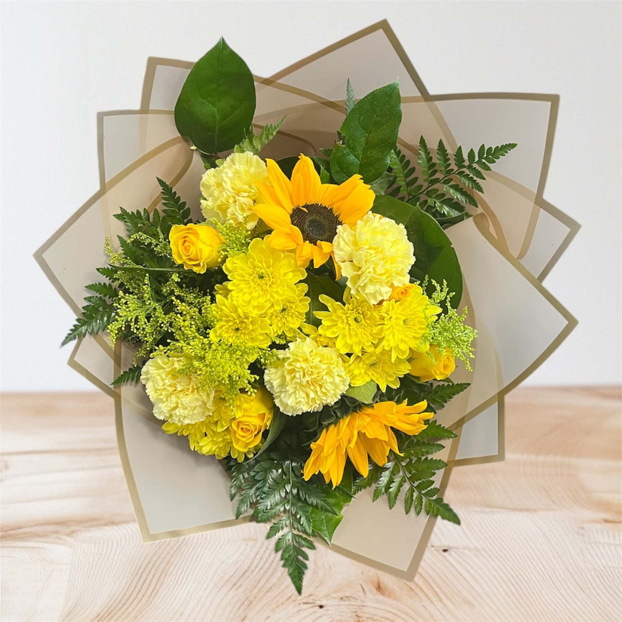 Yellow bouquet with sunflowers, roses, and carnations in tan wrap
