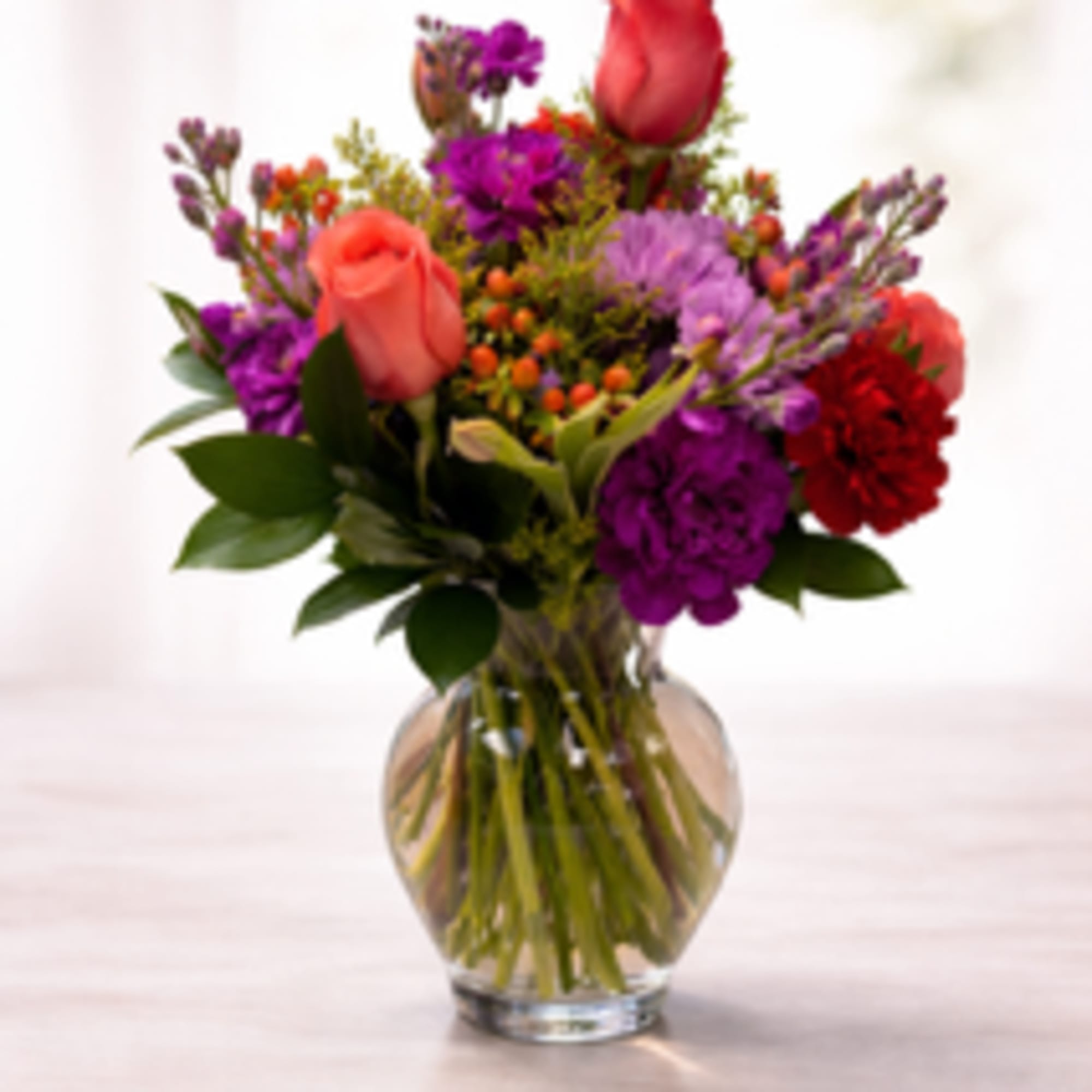 Mixed bouquet of coral roses and purple flowers in a clear glass vase