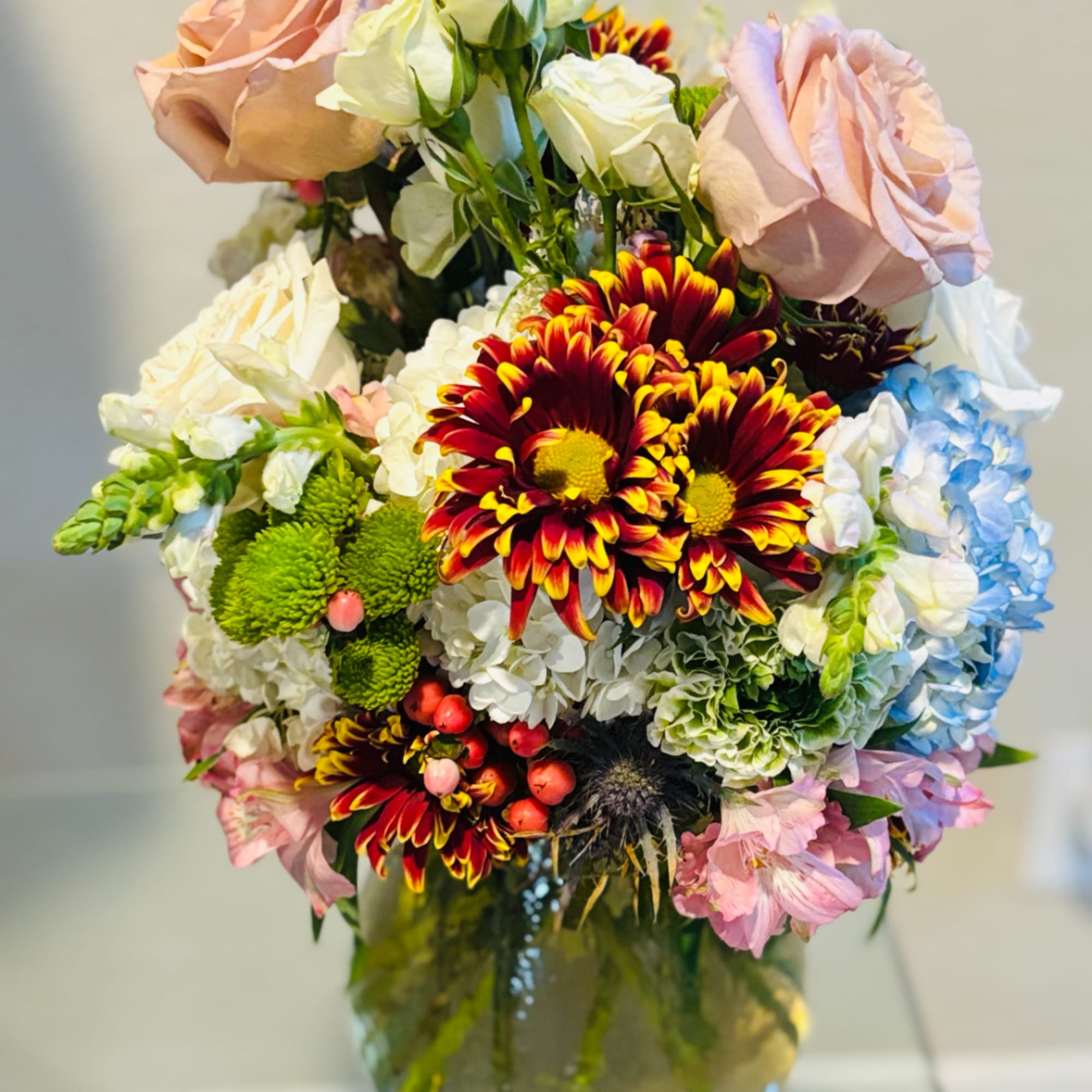 Mixed bouquet of roses, chrysanthemums, and hydrangeas in a glass vase