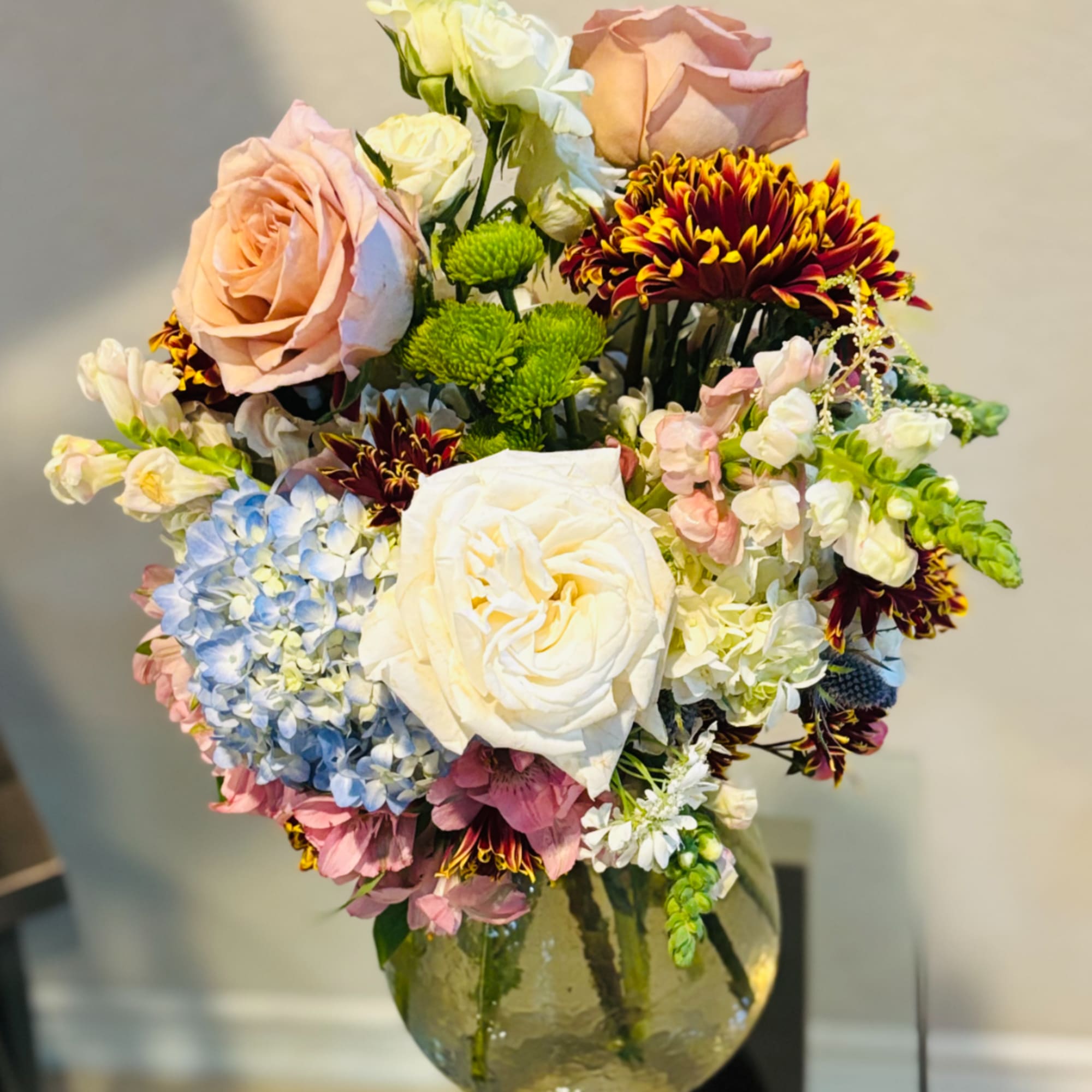Mixed bouquet of roses, hydrangeas, and chrysanthemums in a glass vase