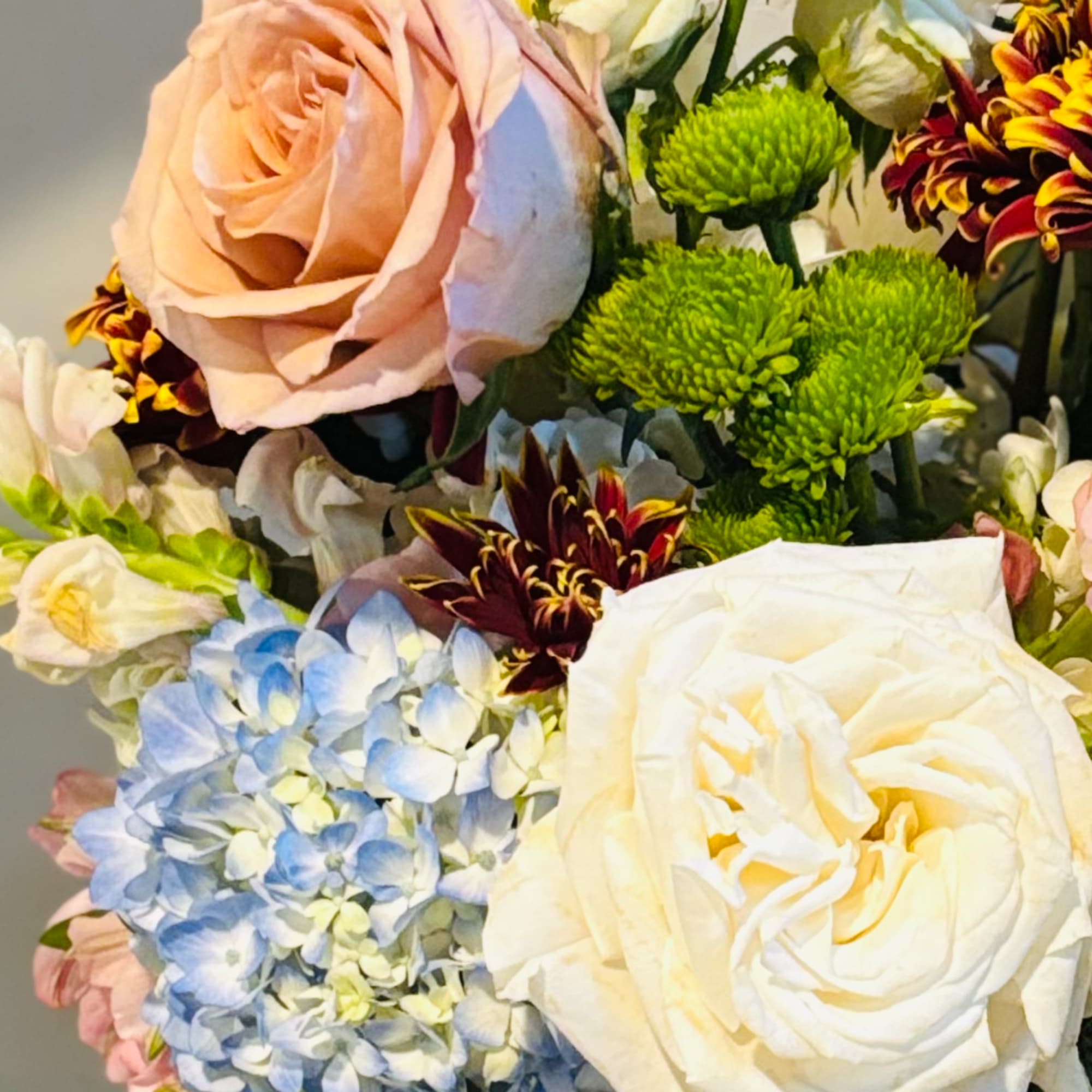 Bouquet of roses, hydrangea, and chrysanthemums in cream, pink, blue, and green.