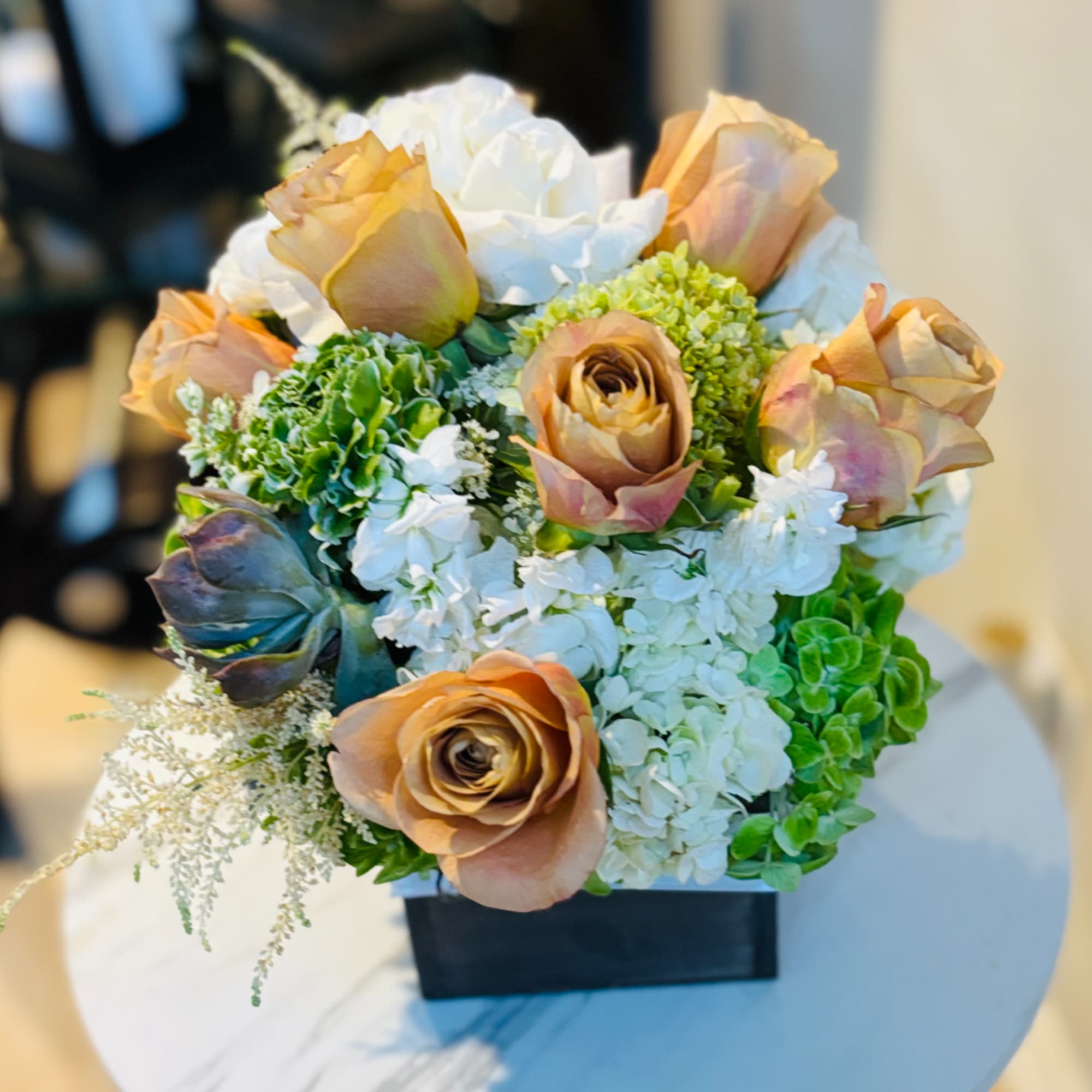 Peach and white roses arranged in a black square vase