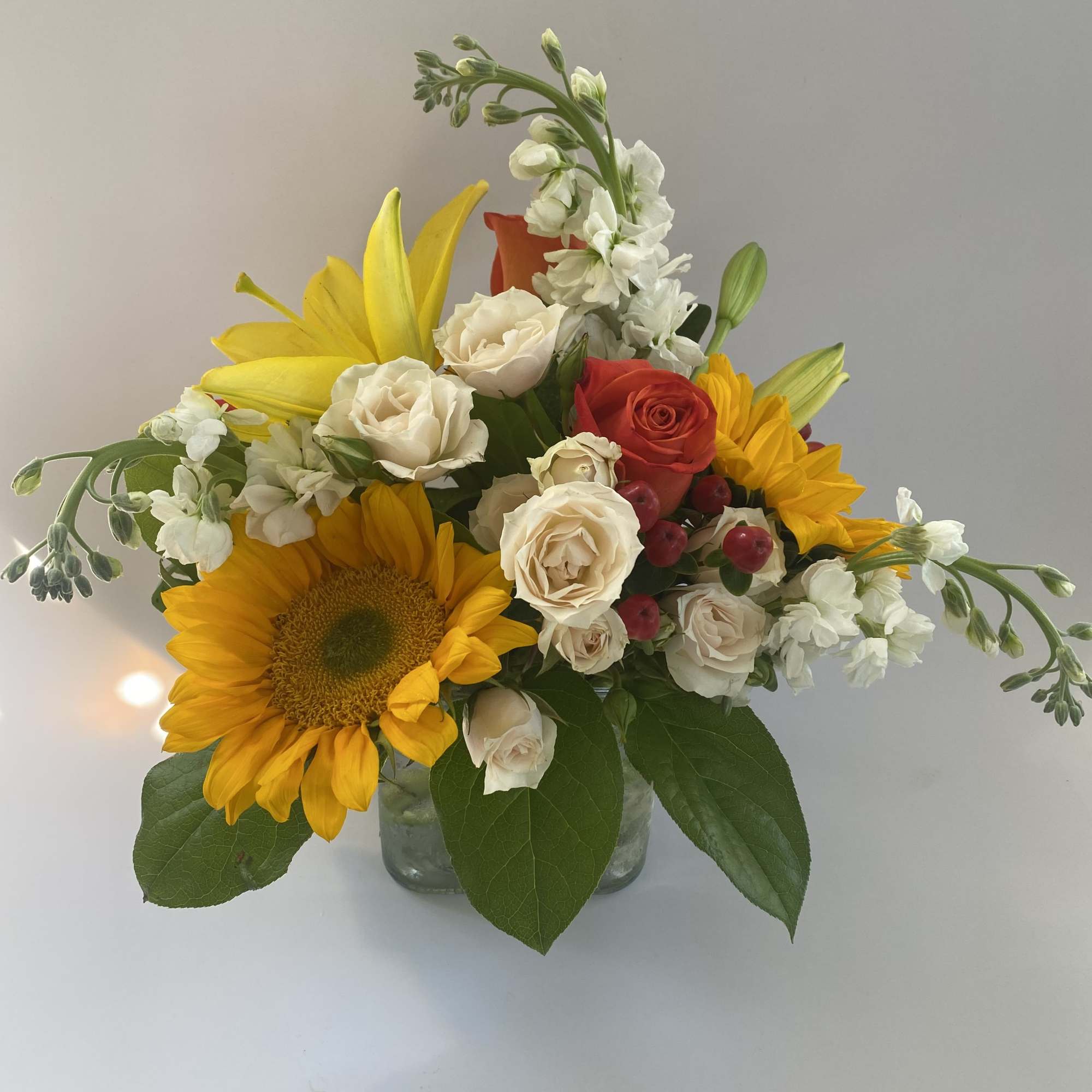 Mixed bouquet with sunflowers, roses, and white blooms in a glass vase