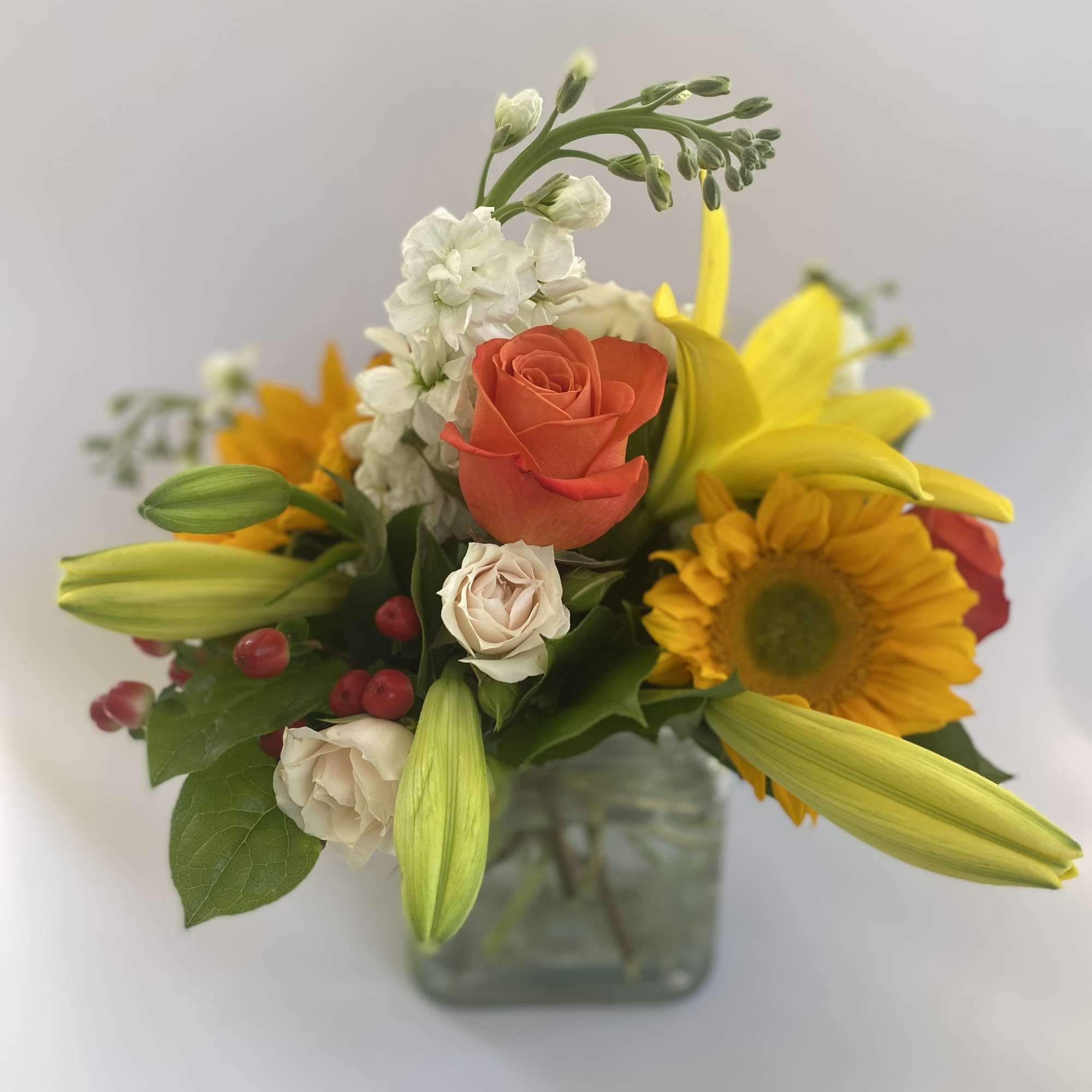 Mixed bouquet with roses, lilies, and a sunflower in a square glass vase
