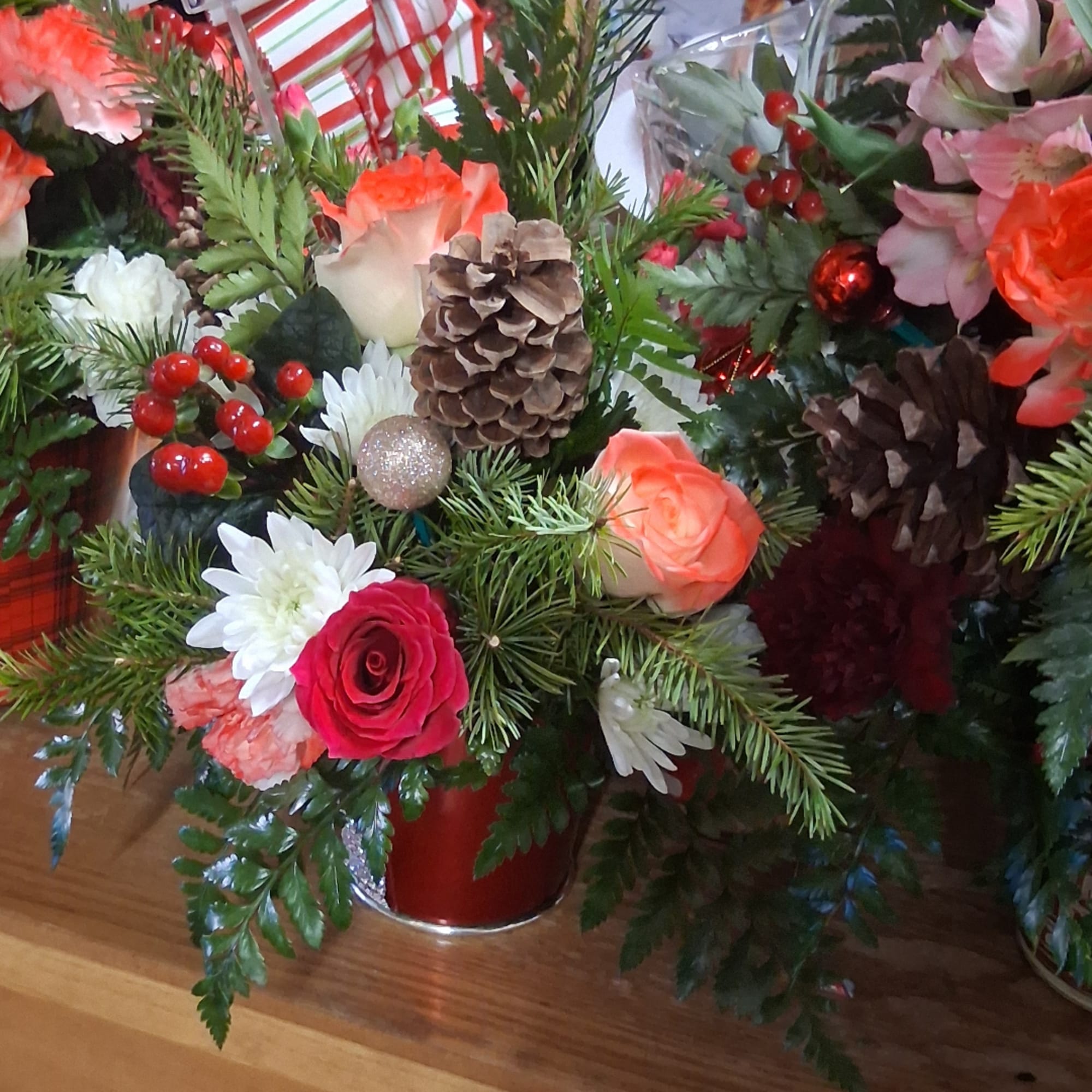 Holiday floral arrangement with roses, daisies, pinecones, and red berries in a red container