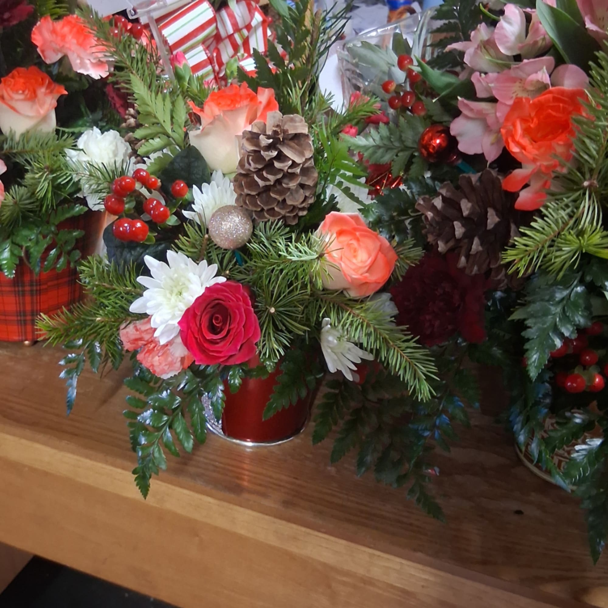 Christmas floral arrangement with roses, daisies, pinecones, and berries in a red container