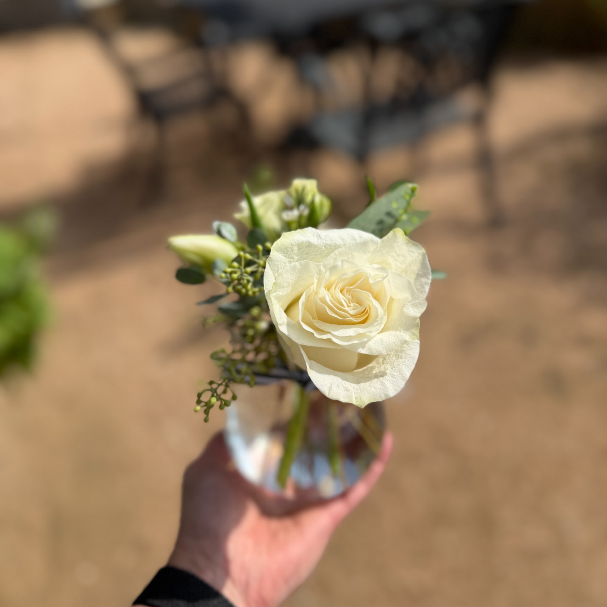 White rose boutonniere in a small glass vase being held by a hand