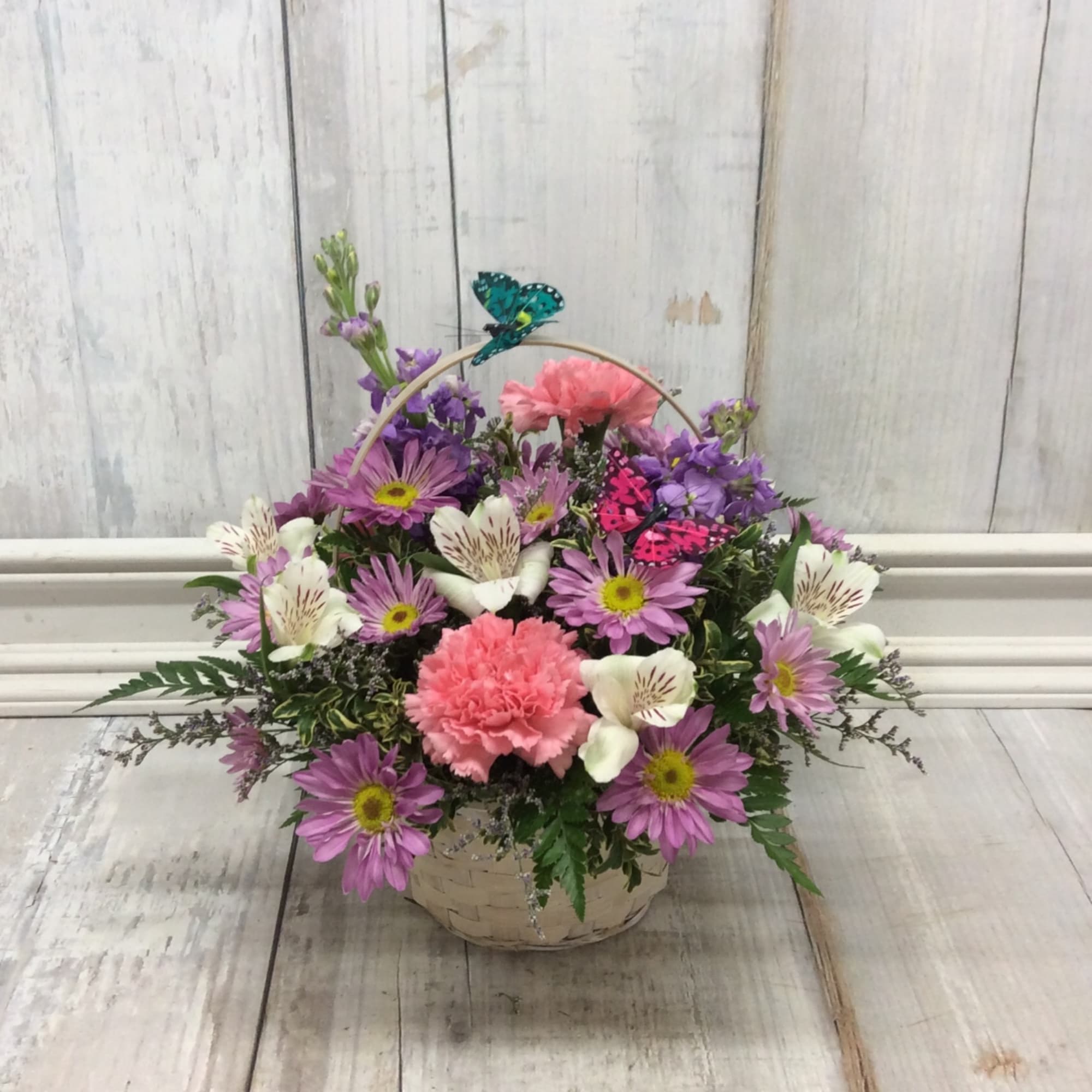Basket arrangement of pink and purple flowers with white blooms and butterfly picks