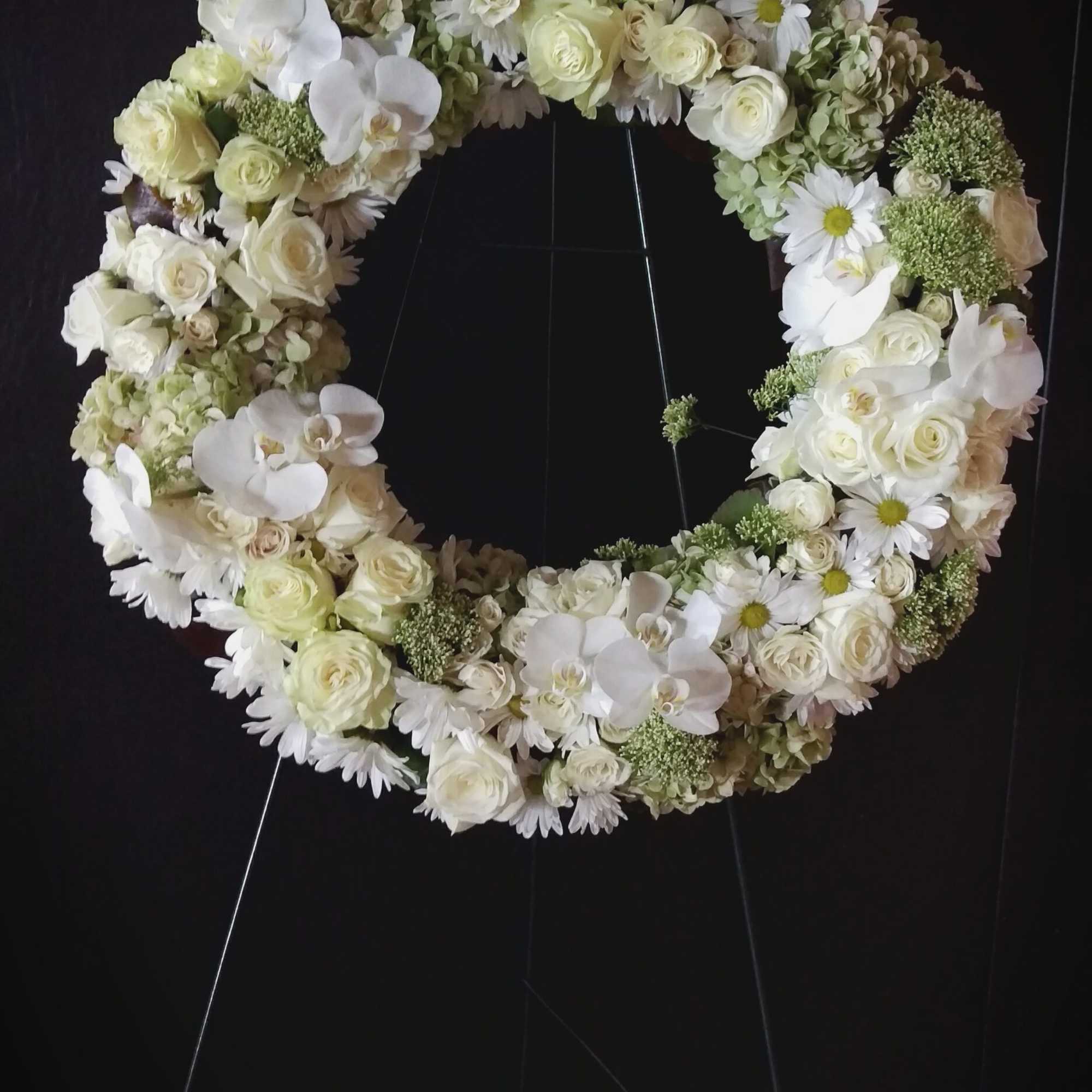 White floral wreath on a stand with roses, orchids, and daisies