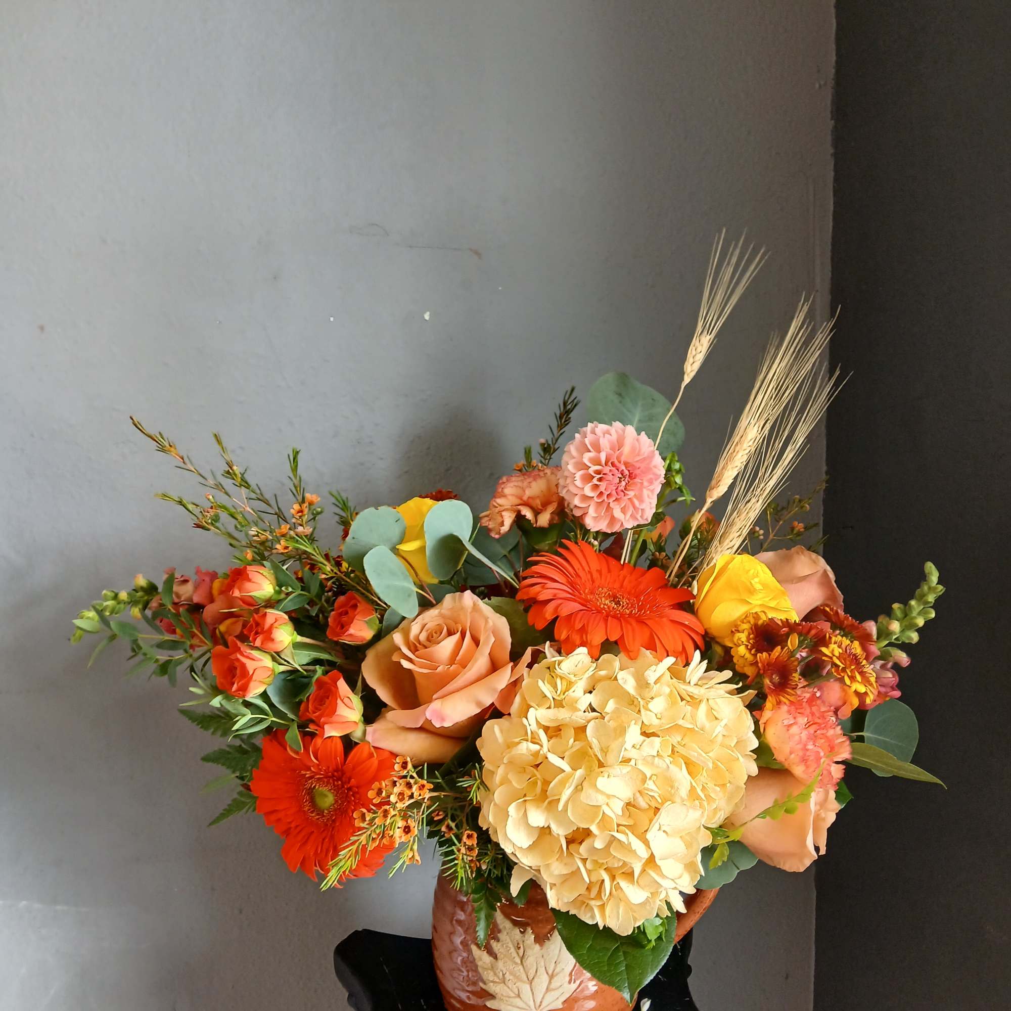 Mixed bouquet of orange, peach, yellow, and pink flowers in a ceramic vase