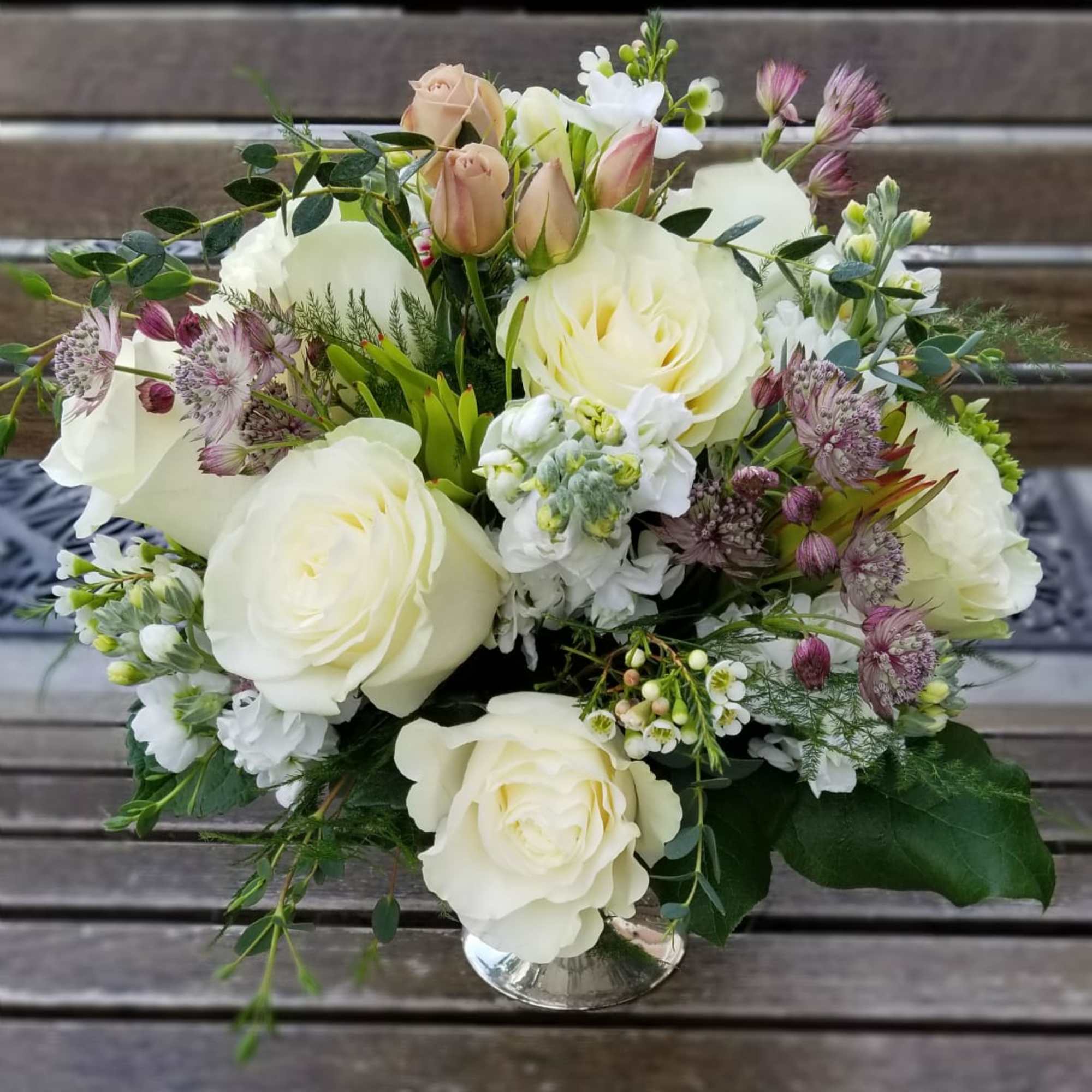 White rose bouquet with small purple flowers in a clear glass vase