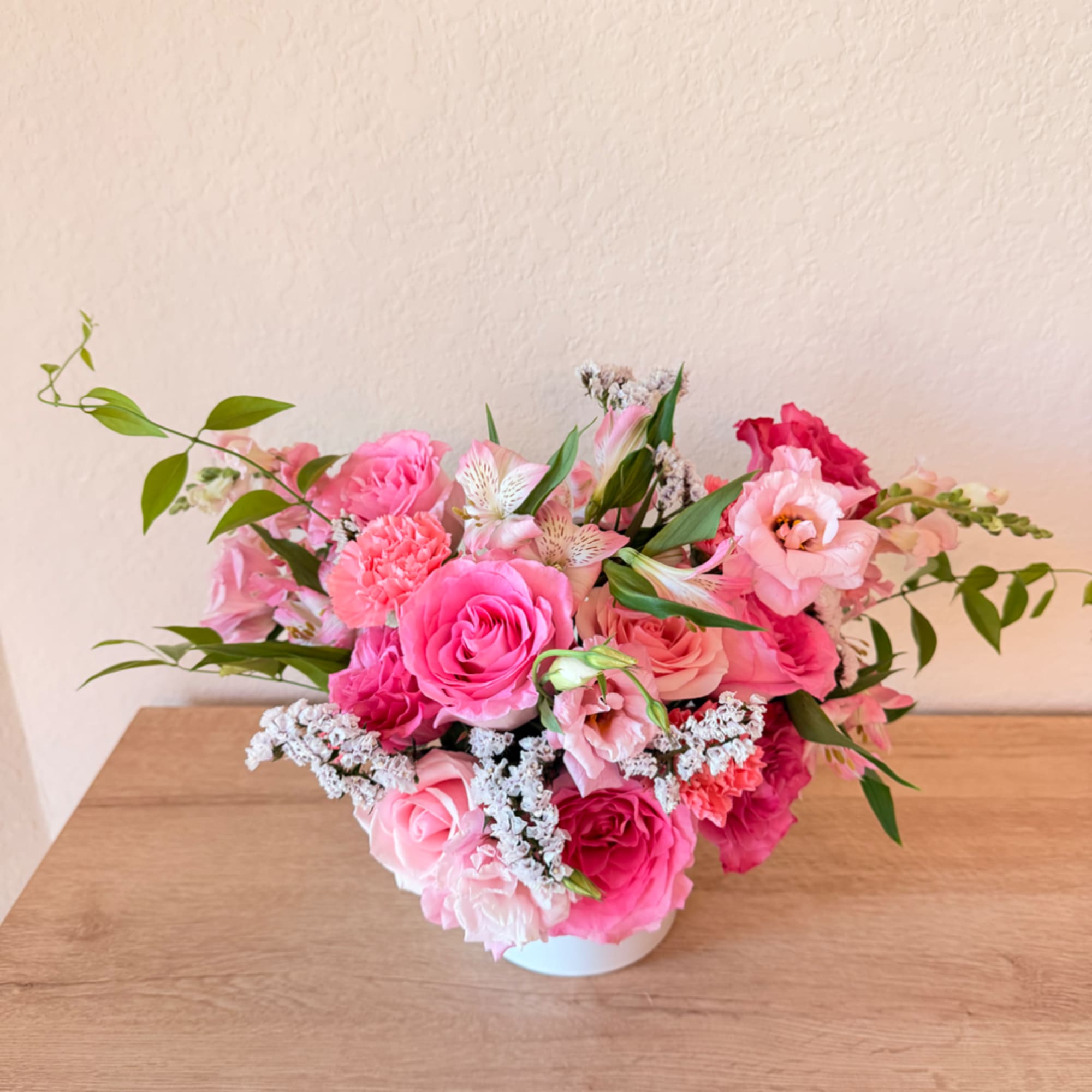 Pink floral arrangement in a white vase on a wooden table
