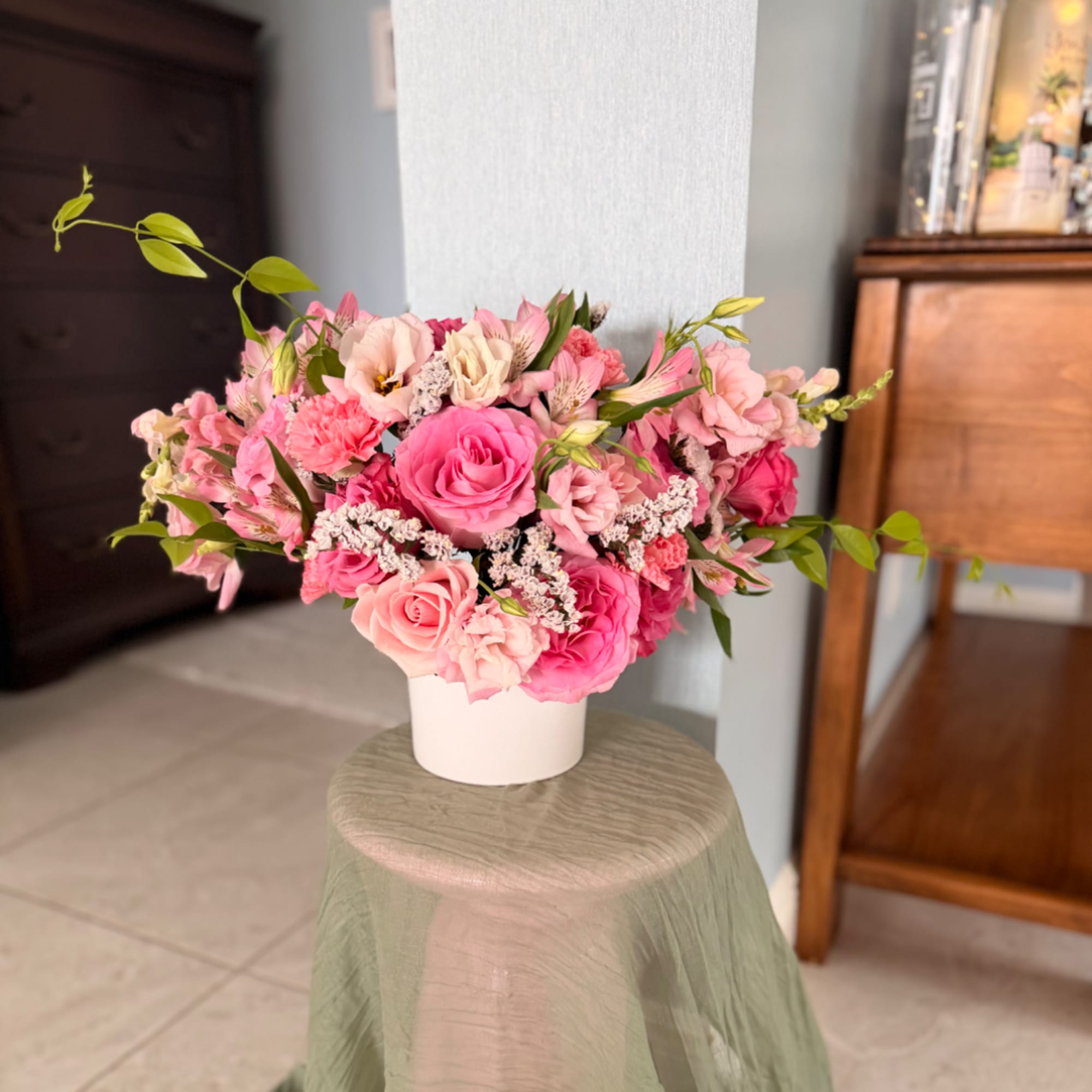 Pink mixed flower arrangement in a white vase on a stool