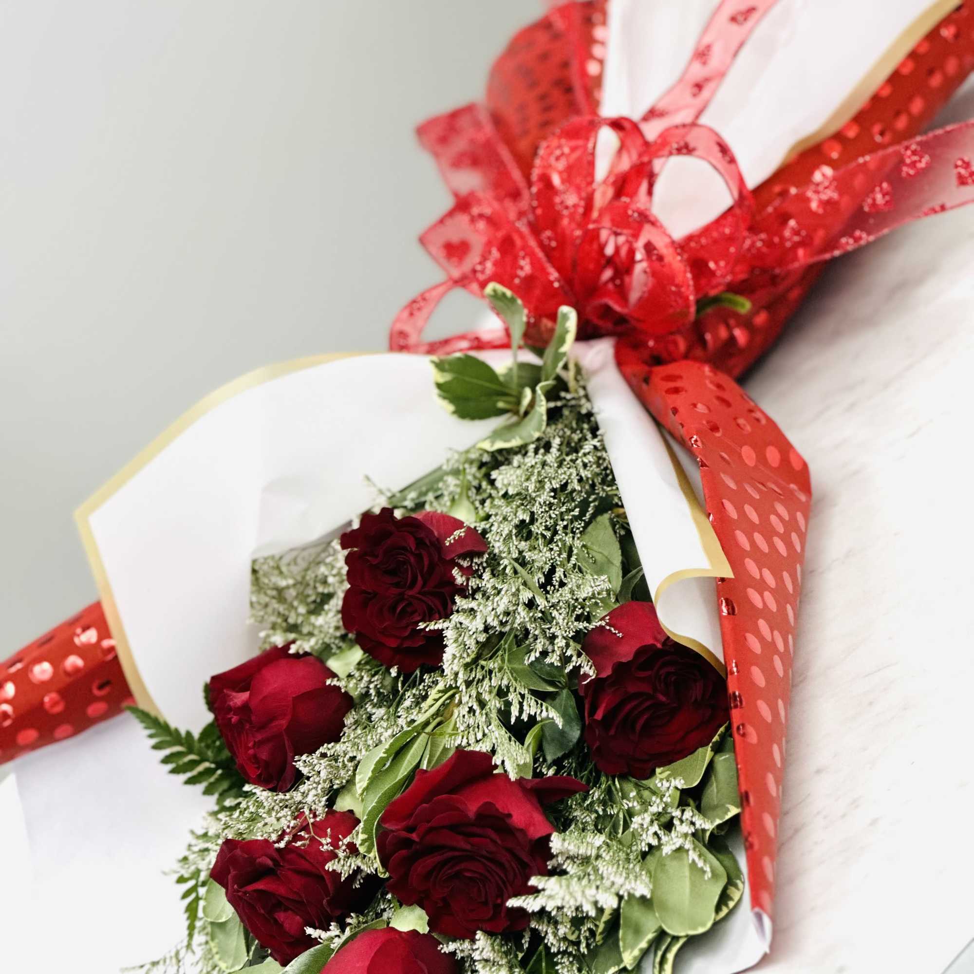 Bouquet of red roses wrapped in white paper with a red ribbon