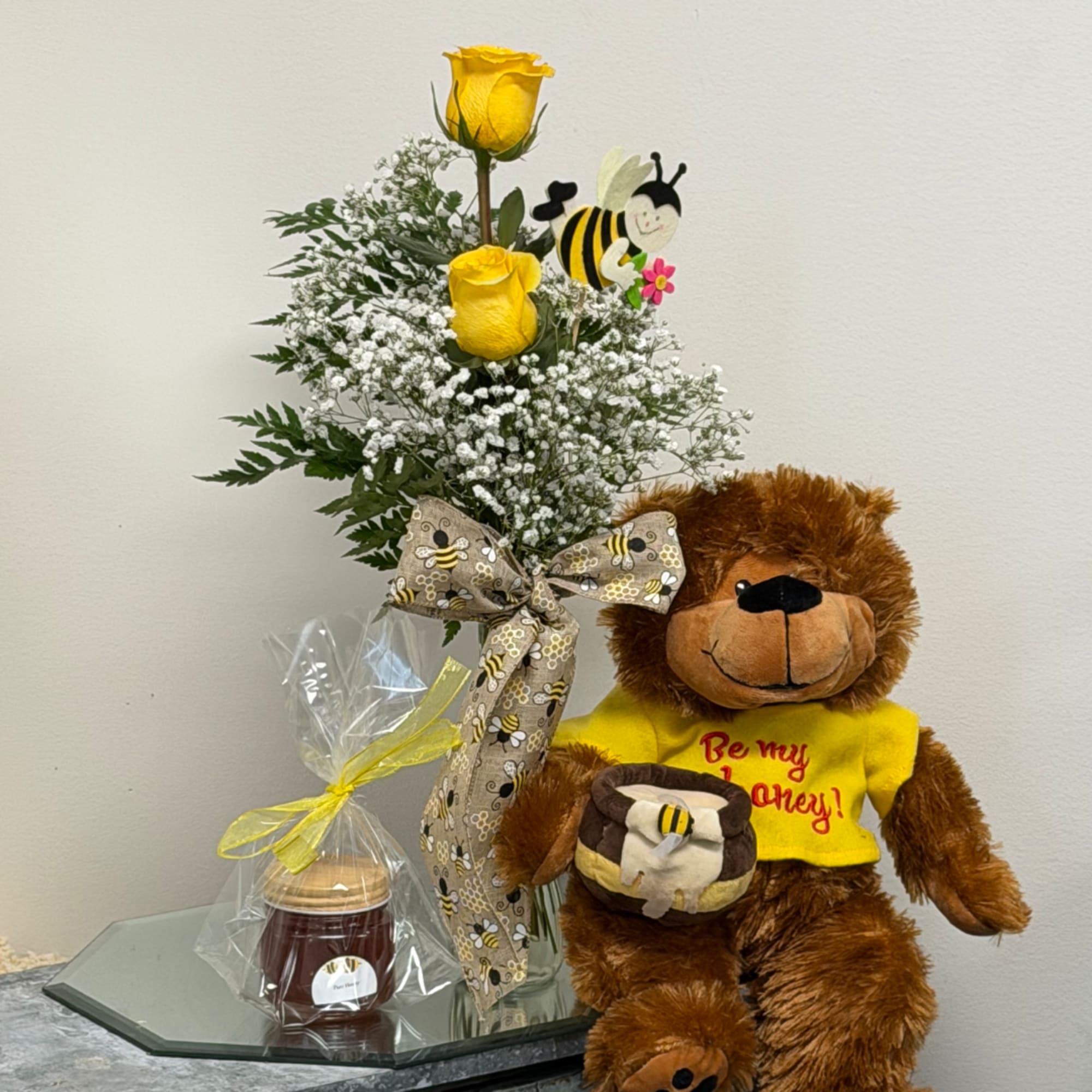 Yellow roses with baby's breath in a vase beside a teddy bear and candle.