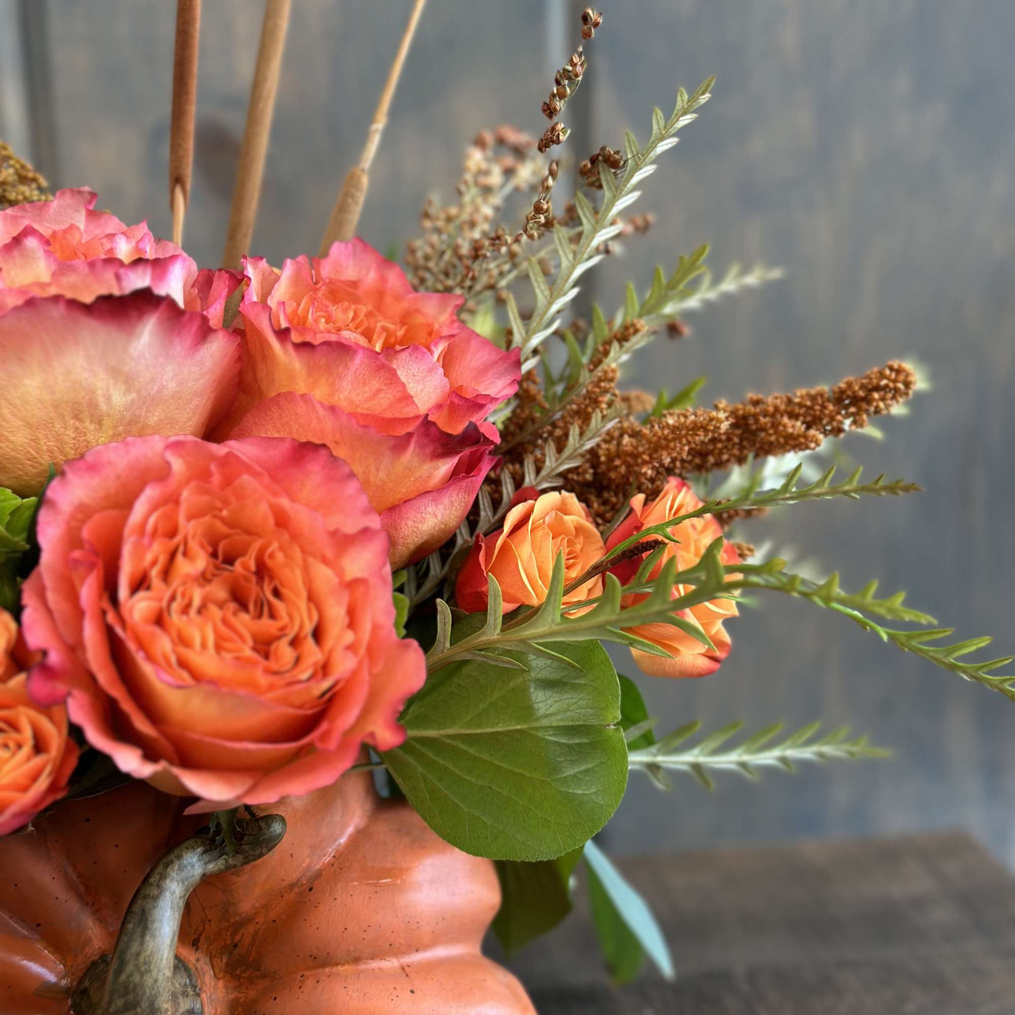 Orange roses in a pumpkin-shaped vase with dried accents