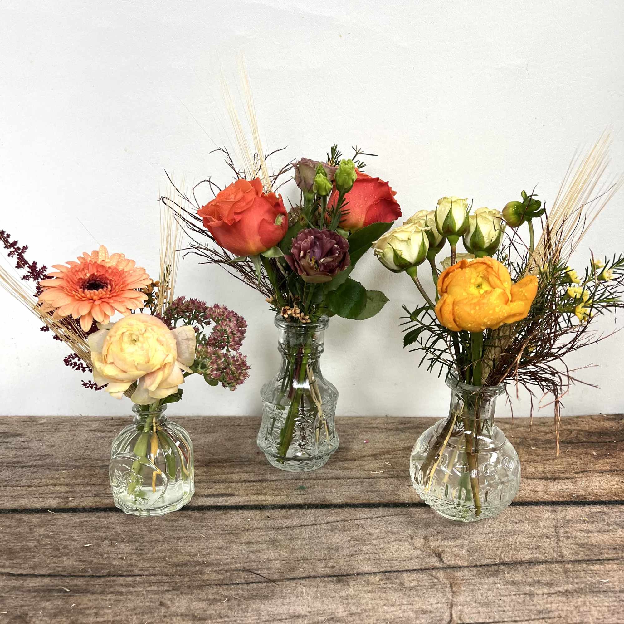 Three small flower arrangements in clear glass vases on a wooden surface