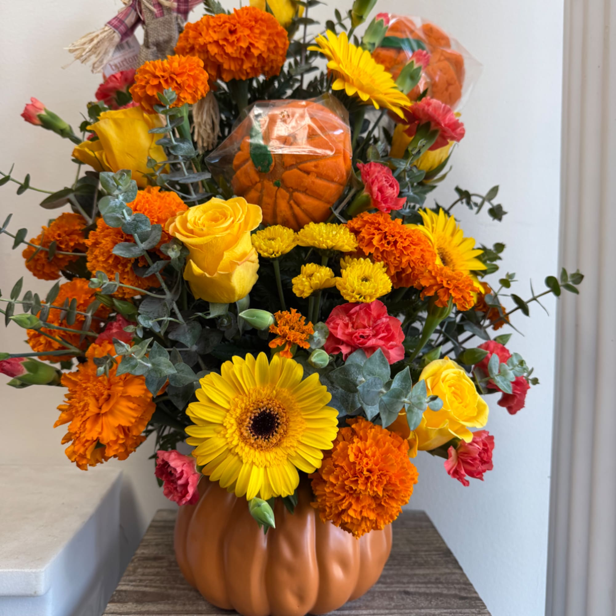 Autumn bouquet with yellow roses, gerbera daisies, and orange marigolds in a pumpkin vase.