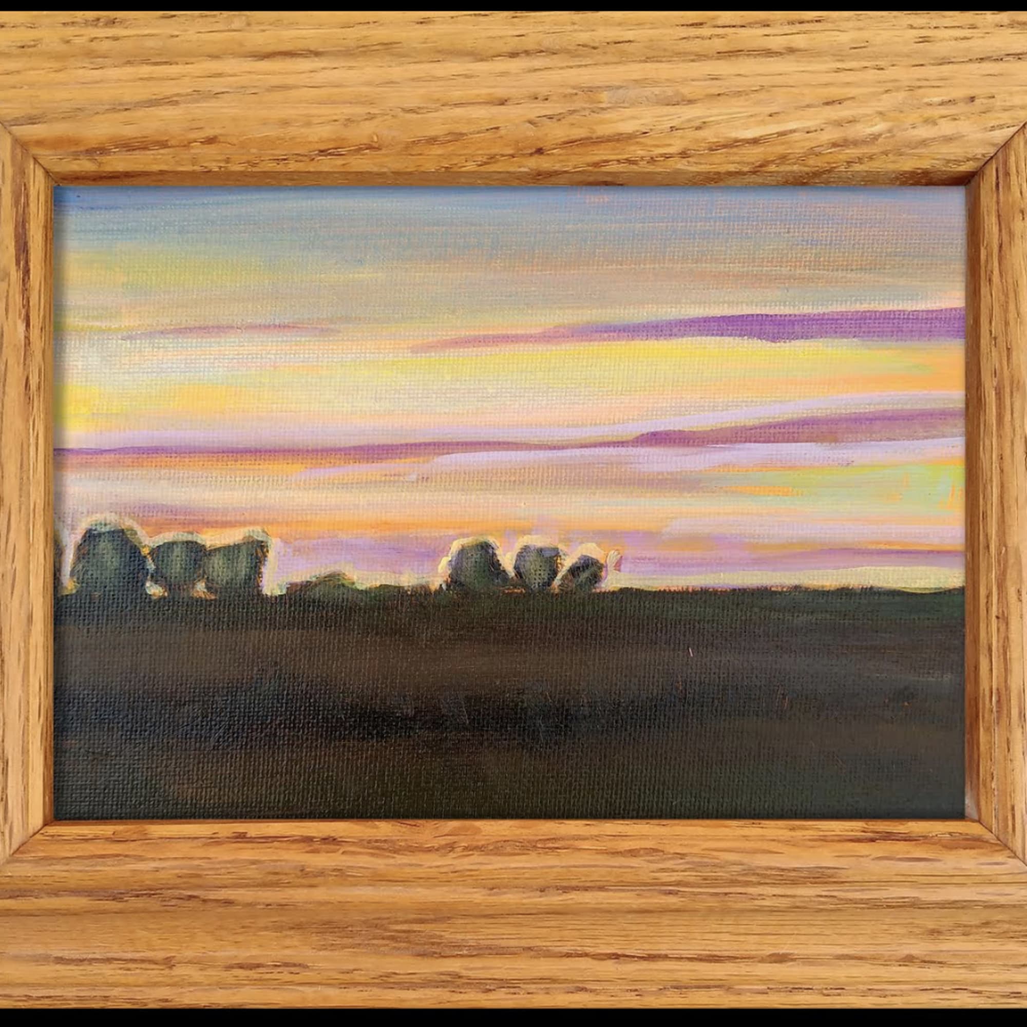 Framed landscape painting of a colorful sunset over a dark field