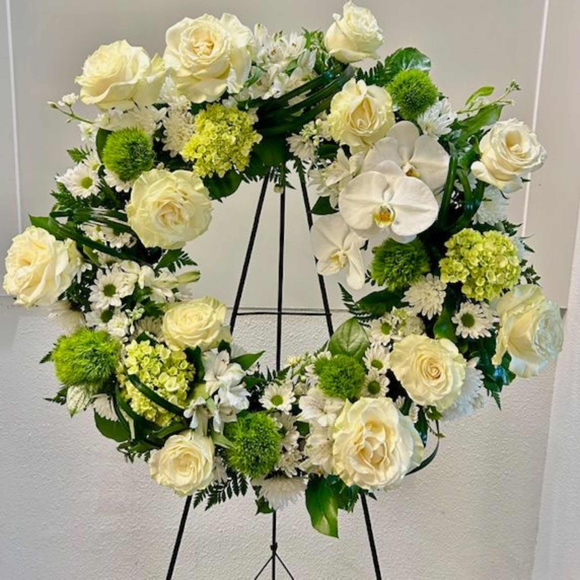 White floral wreath on a black stand with roses and orchids
