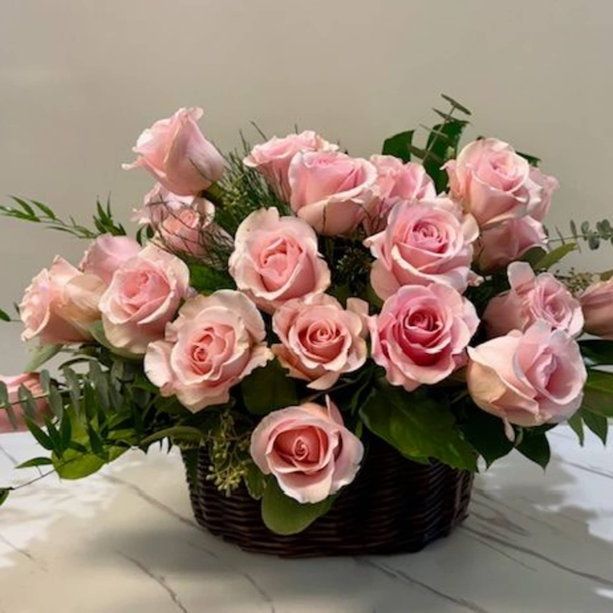 Pink roses arranged in a dark basket with greenery