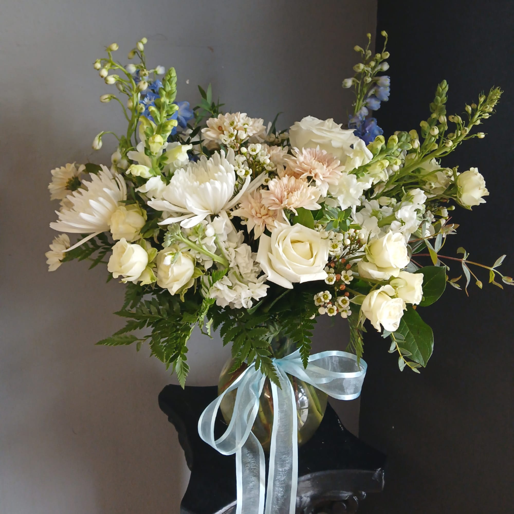 White and pale peach flowers arranged in a glass vase with a blue ribbon.