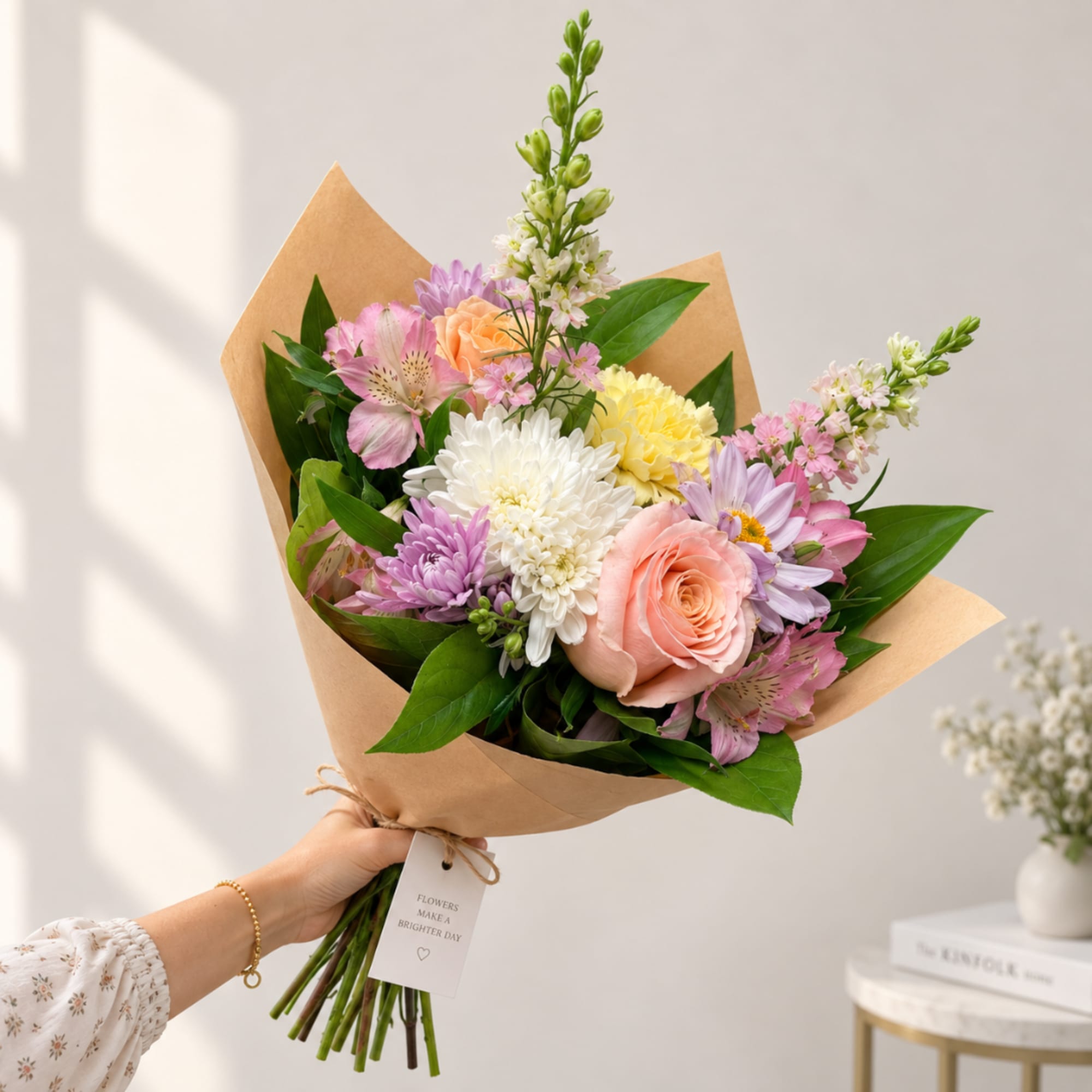 Handheld bouquet of mixed pastel flowers wrapped in kraft paper