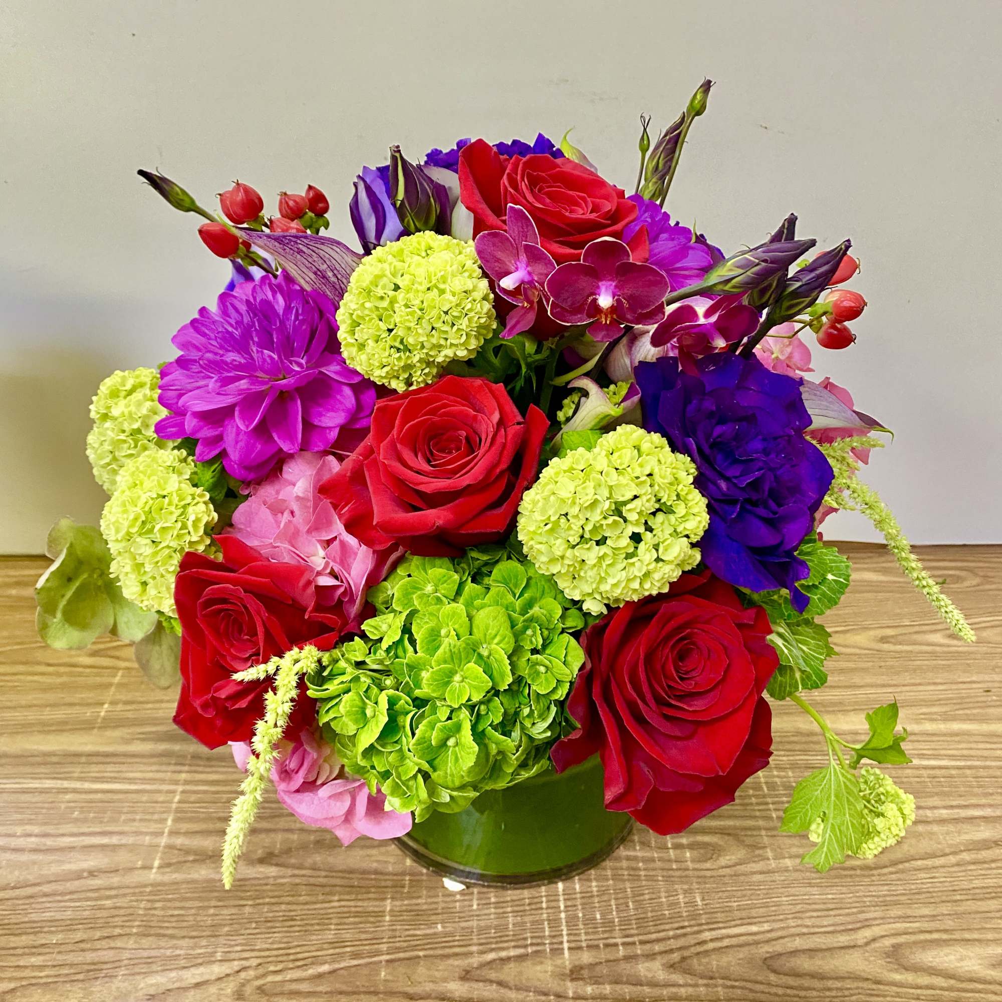 Bouquet of red roses, purple blooms, and green hydrangeas in a glass vase