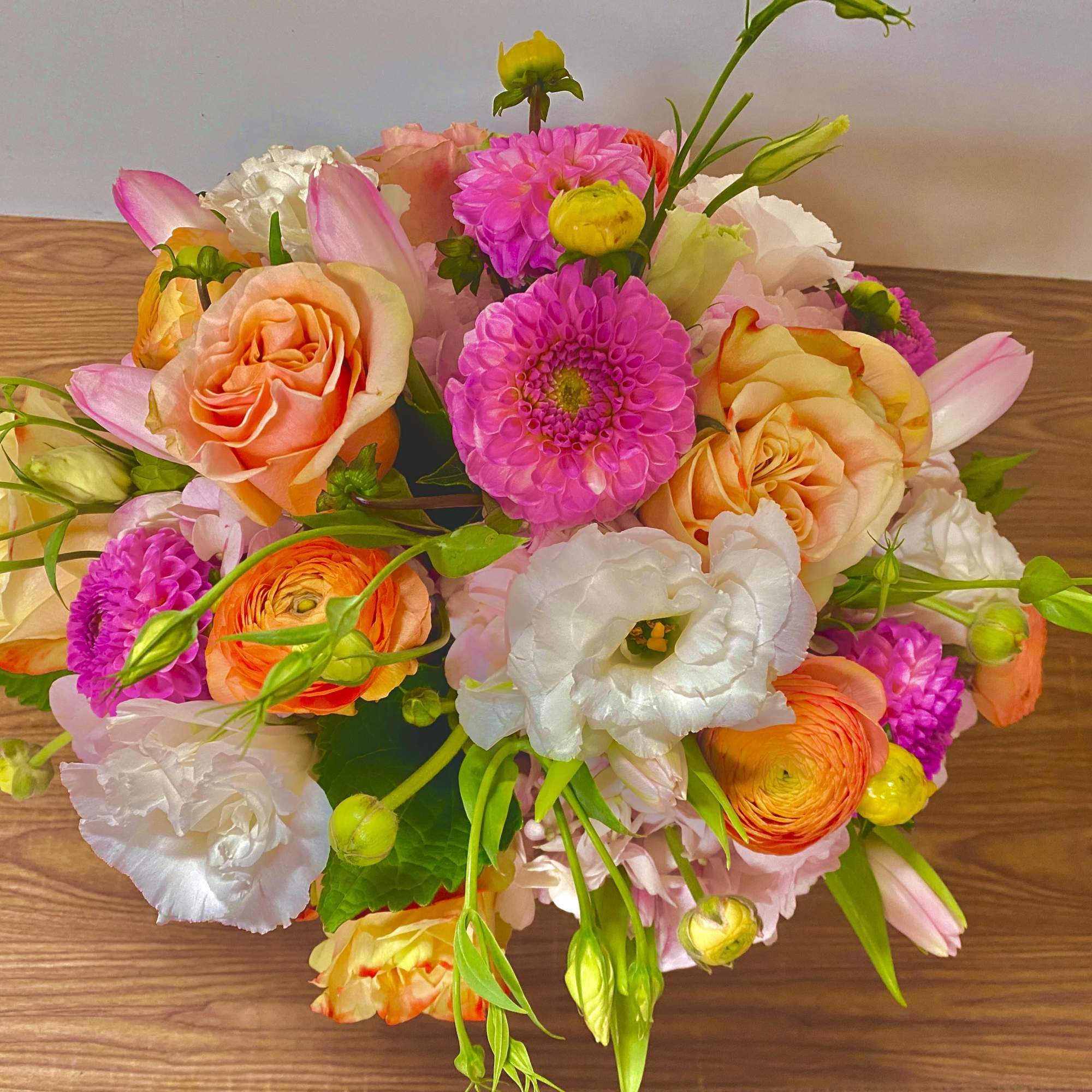 Mixed bouquet of pink, peach, white, and orange flowers on a wooden surface