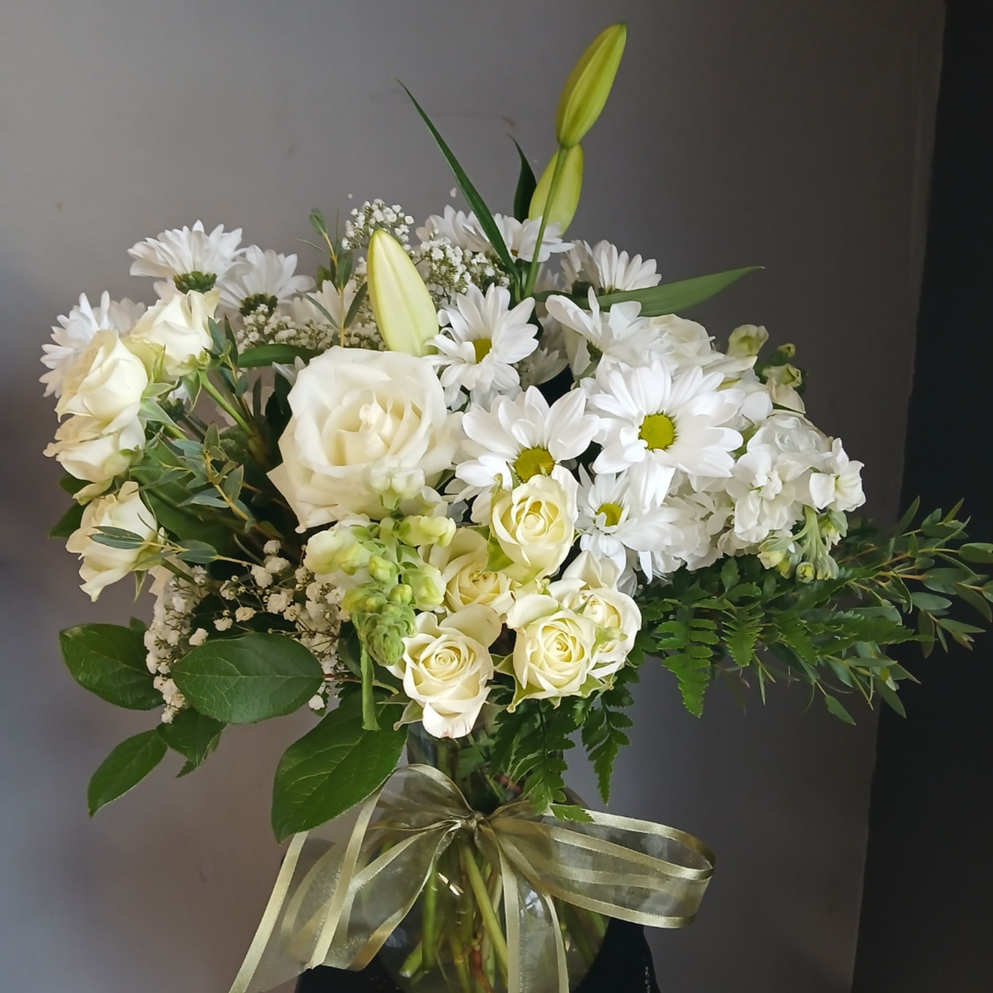 White roses and daisies arranged in a glass vase with a ribbon.