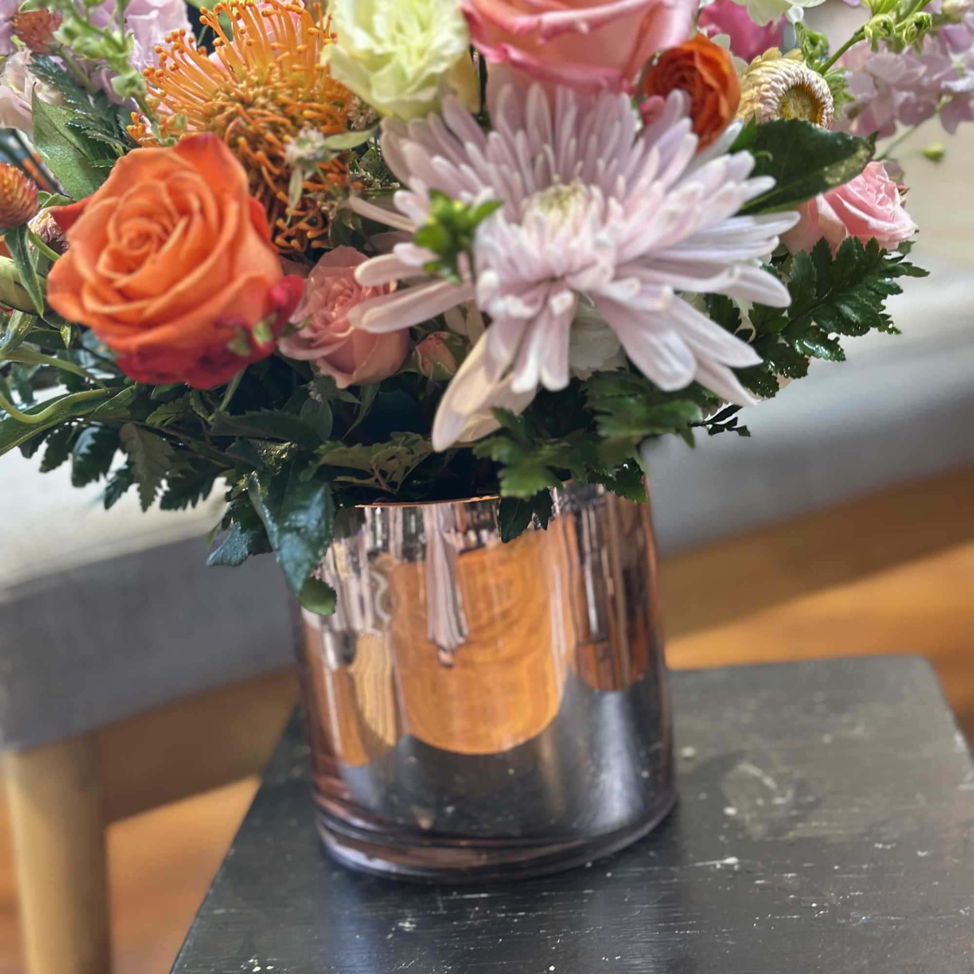 Colorful arrangement of pink and orange flowers with protea in a reflective rose-gold cylinder vase