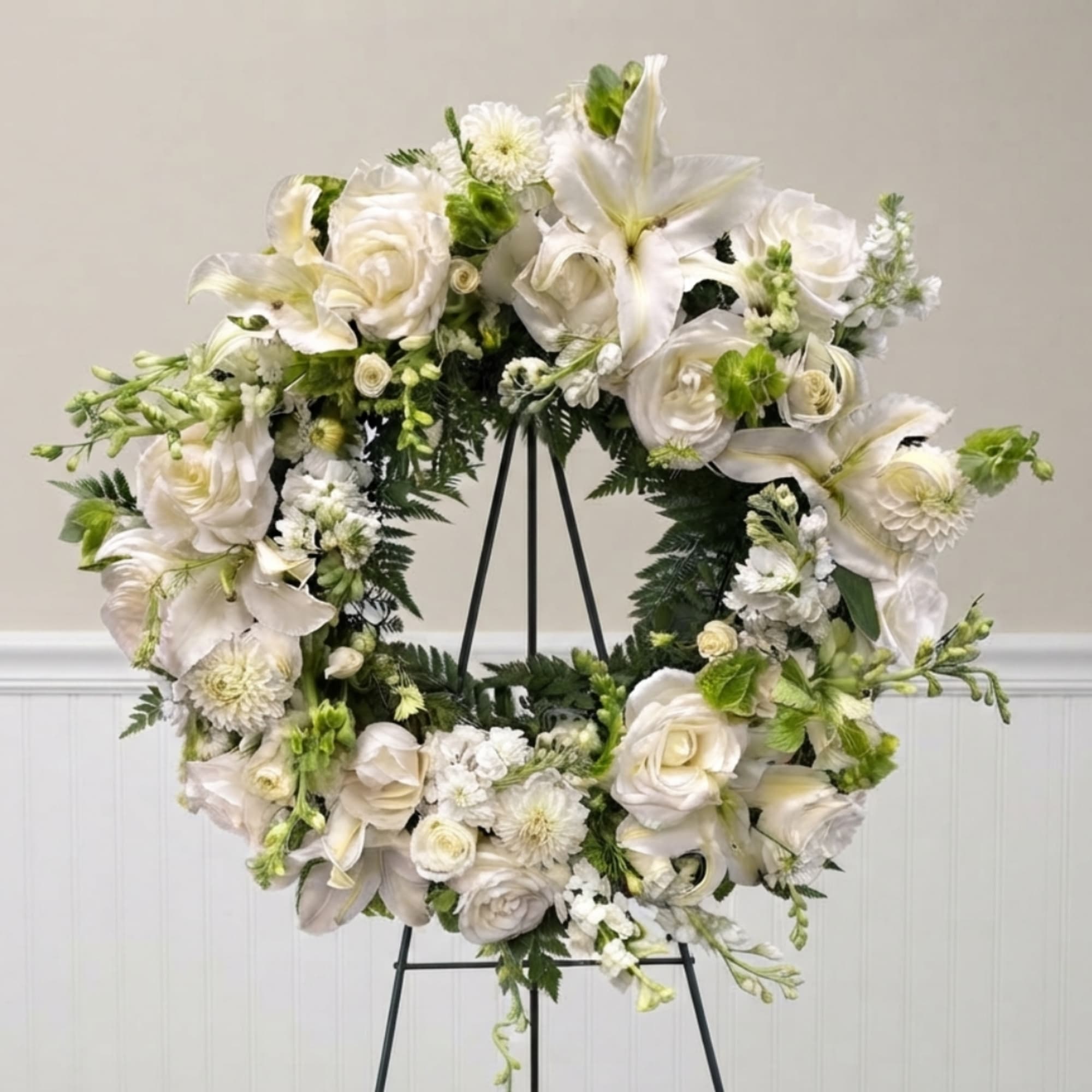 White floral wreath on a black stand with roses and lilies