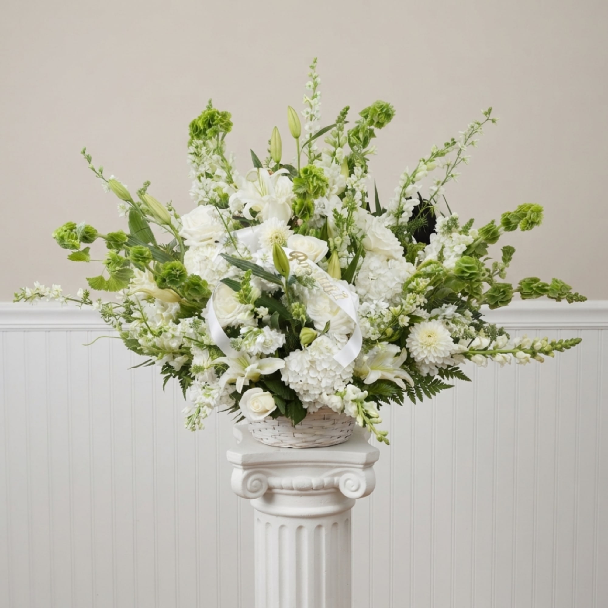 White floral arrangement in a basket with a ribbon on a pedestal