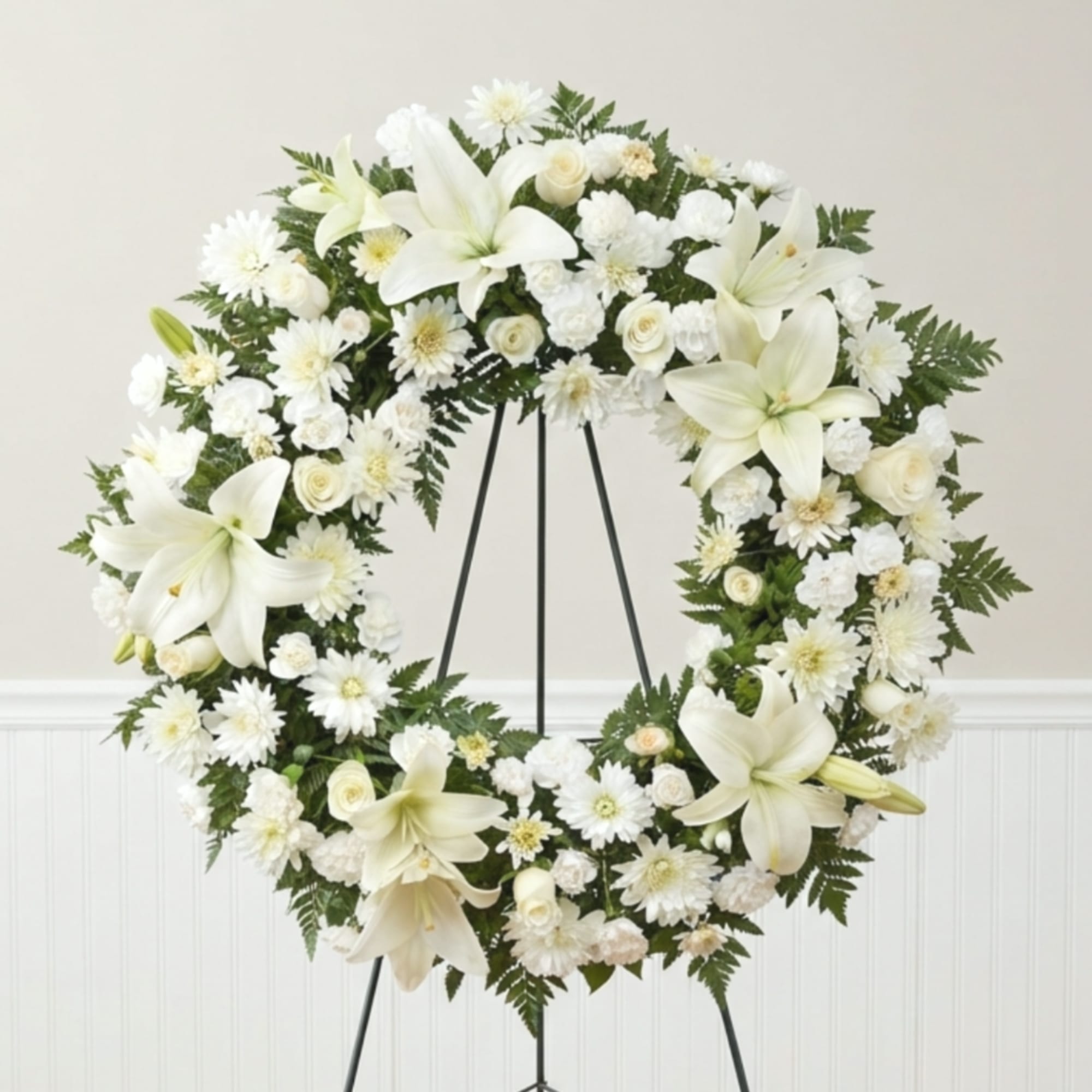 White floral wreath on a black stand with lilies and daisies