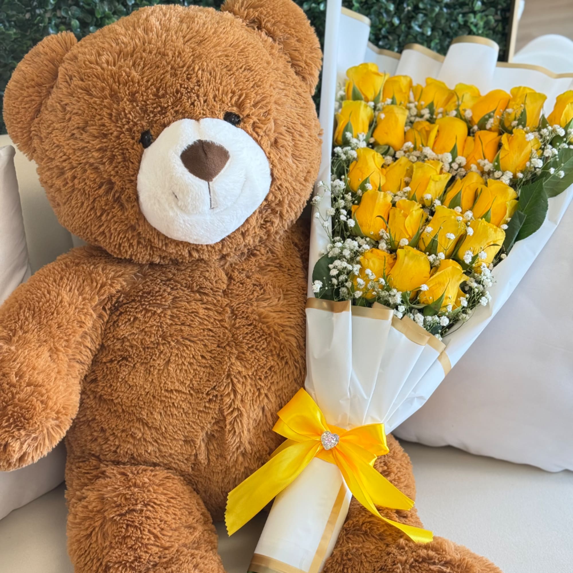 Brown teddy bear beside a bouquet of yellow roses wrapped in white paper