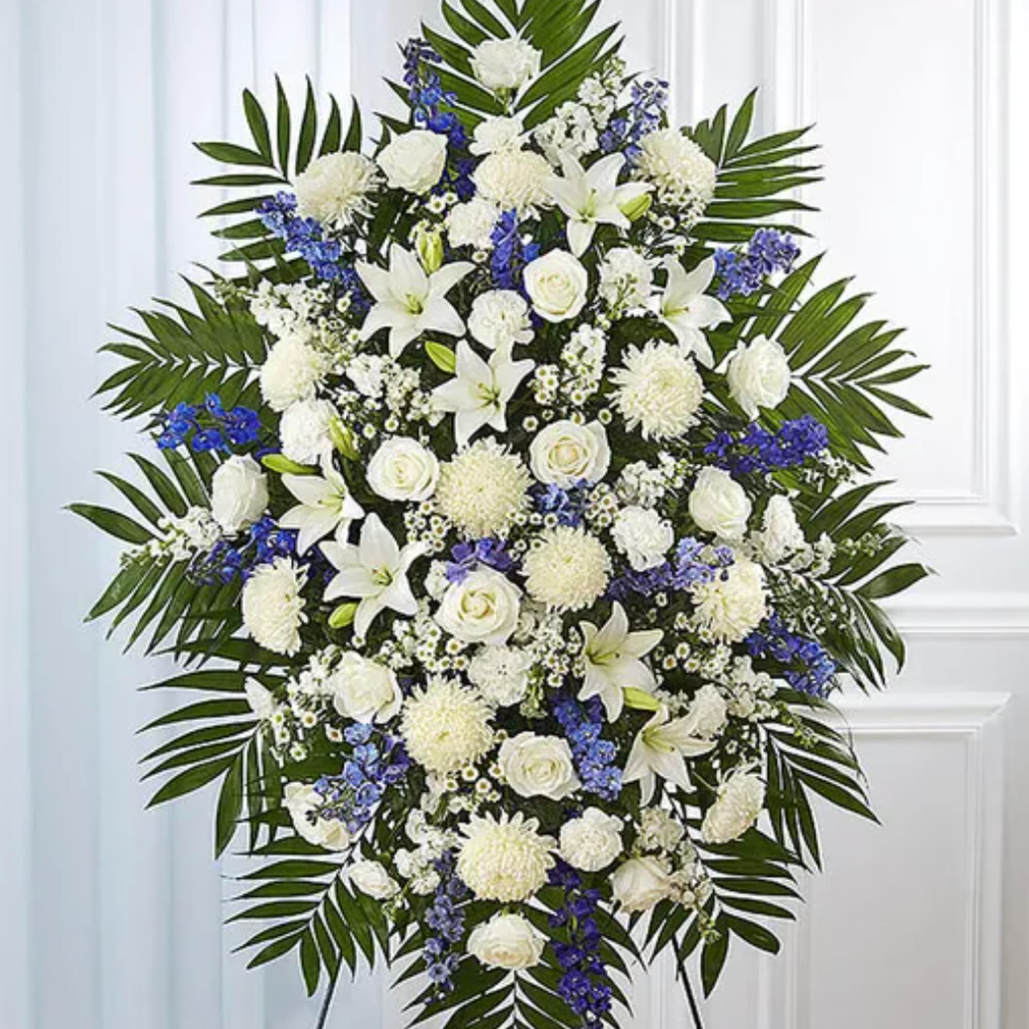 Large white and blue funeral spray with palm fronds on an easel